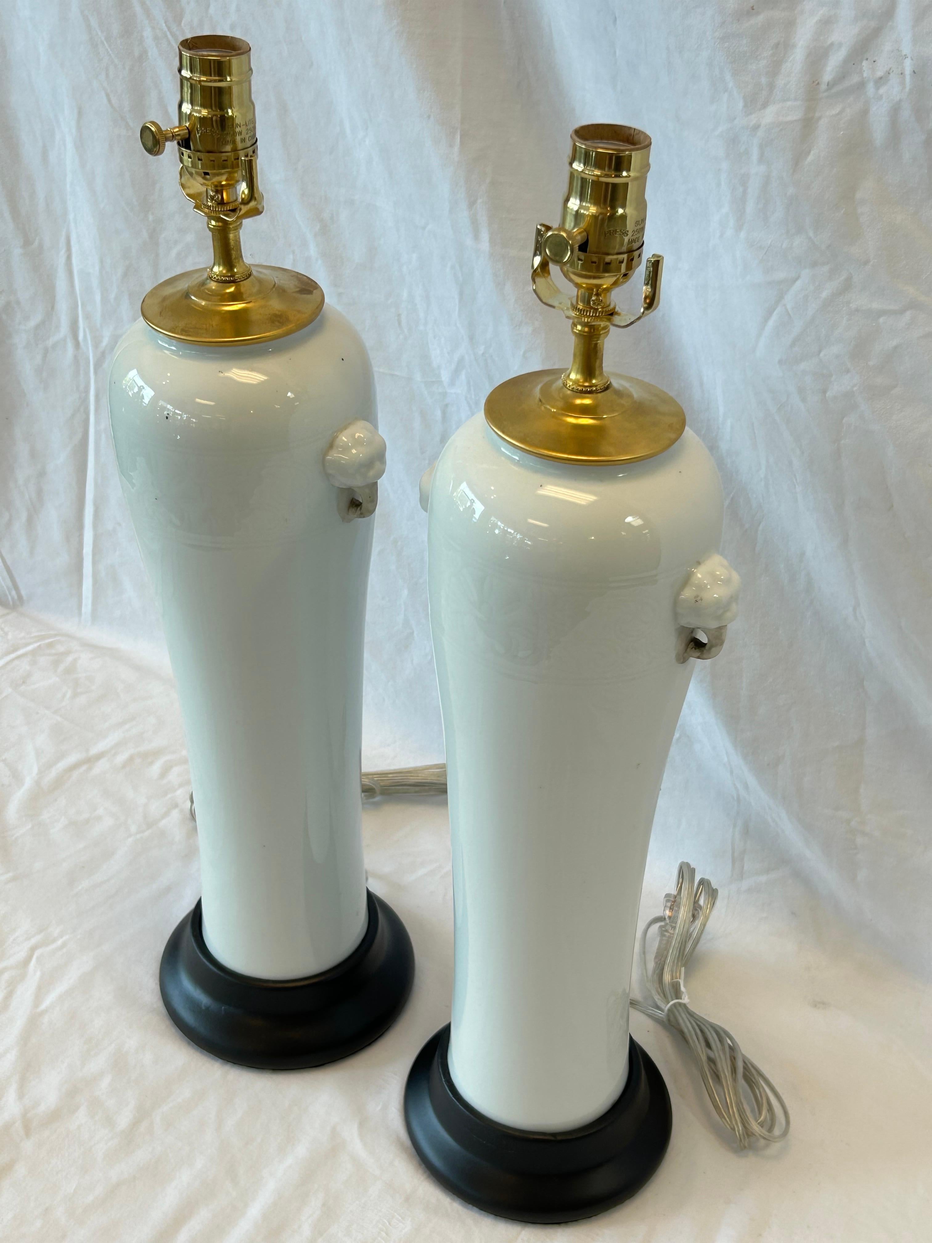 A tall and slender pair of creamy white elongated sleeve or inverted baluster form Dehua style Blanc de Chine Chinese table lamps with black bases, recently rewired. The impressed and incised decoration is a wide band around the upper portion of