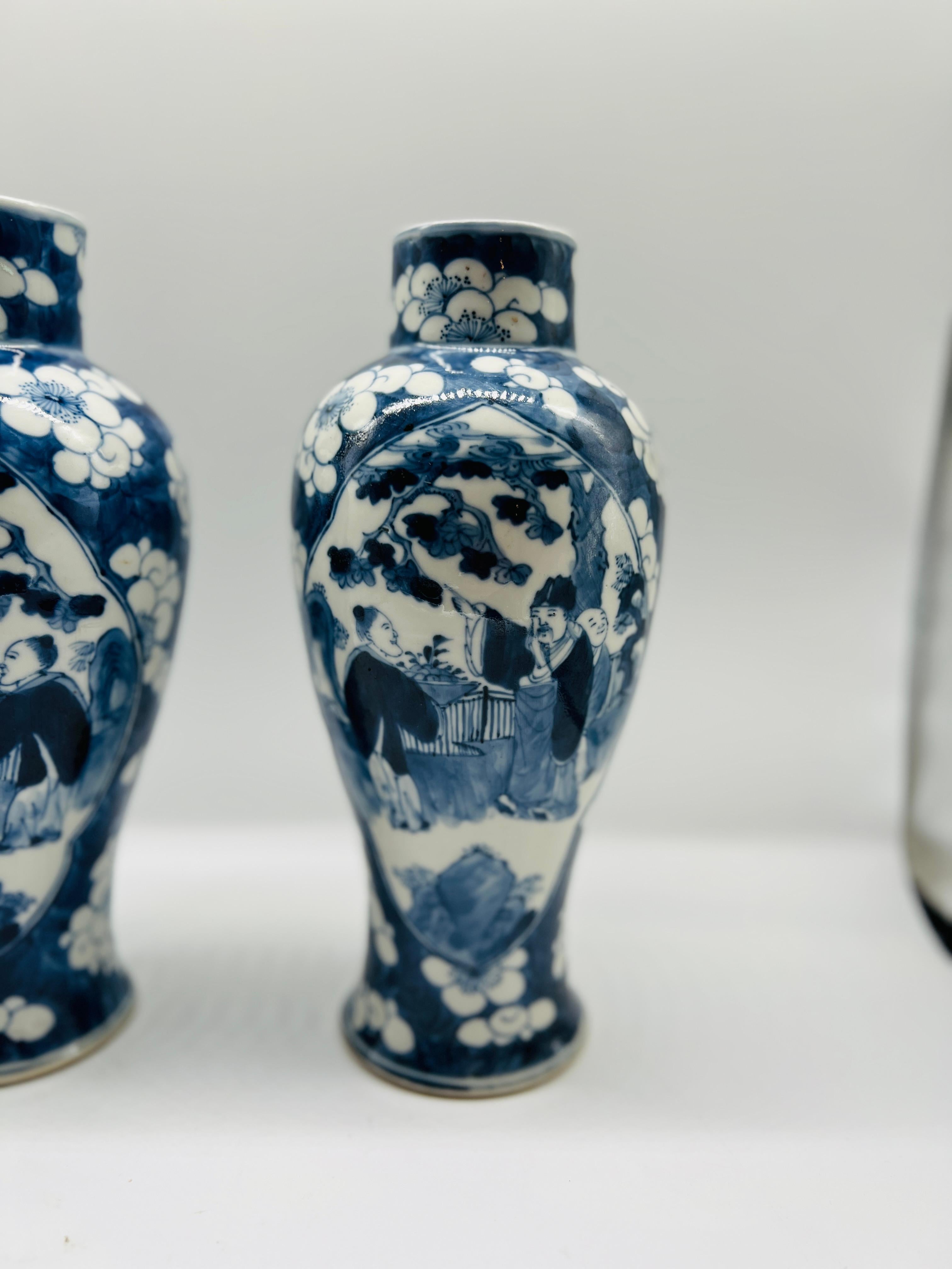 This exquisite pair of Chinese export blue and white vases features finely painted figural scenes, each framed within large, detailed windows surrounded by lush floral blossoms. The intricate floral motifs complement the central figures, creating a