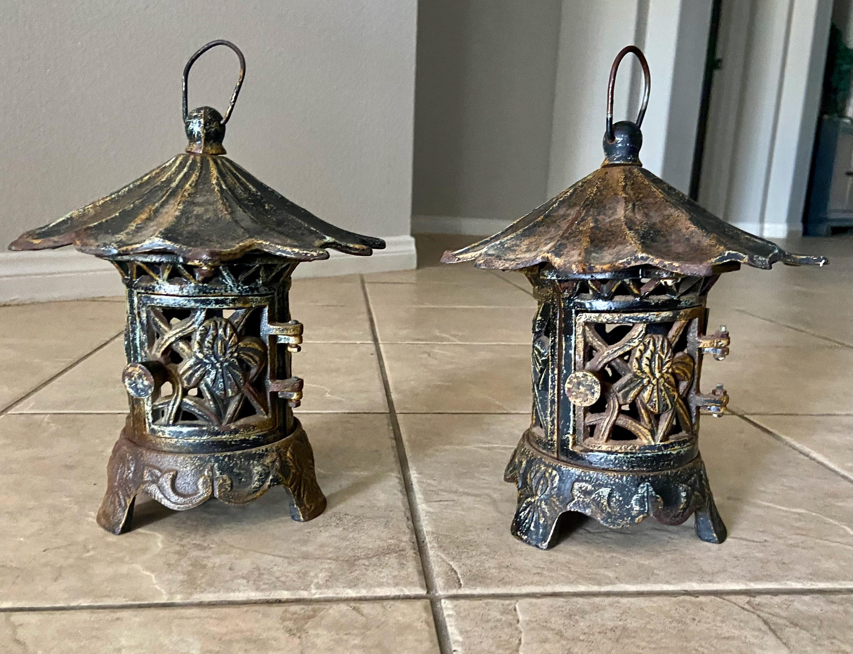 Pair of antique Chinese heavy cast iron pagoda garden lanterns with original patina, having a handle for hanging, hinged cage door and openwork screen sides, adorned with traditional Asian motif detailing. Single tea candle holder interior. Stamped