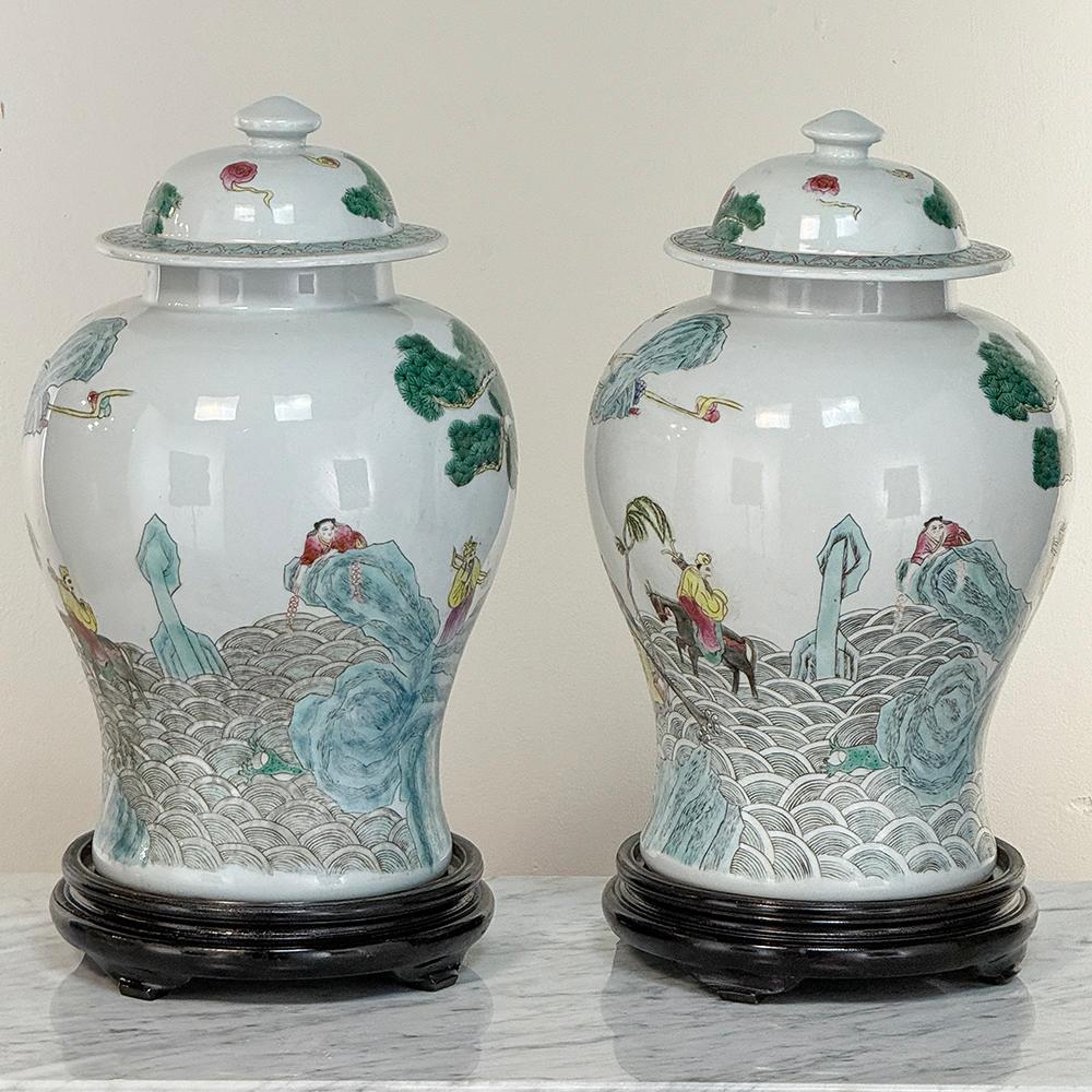 Ein Paar antike chinesische Porzellan-Urnen mit Deckel und Holzsockel sind ein reizvolles Design, mit klassischer Form und exquisiten Juwelenfarben, die mit talentierter Kunstfertigkeit ausgedrückt werden, um eine Vielzahl von Charakteren in