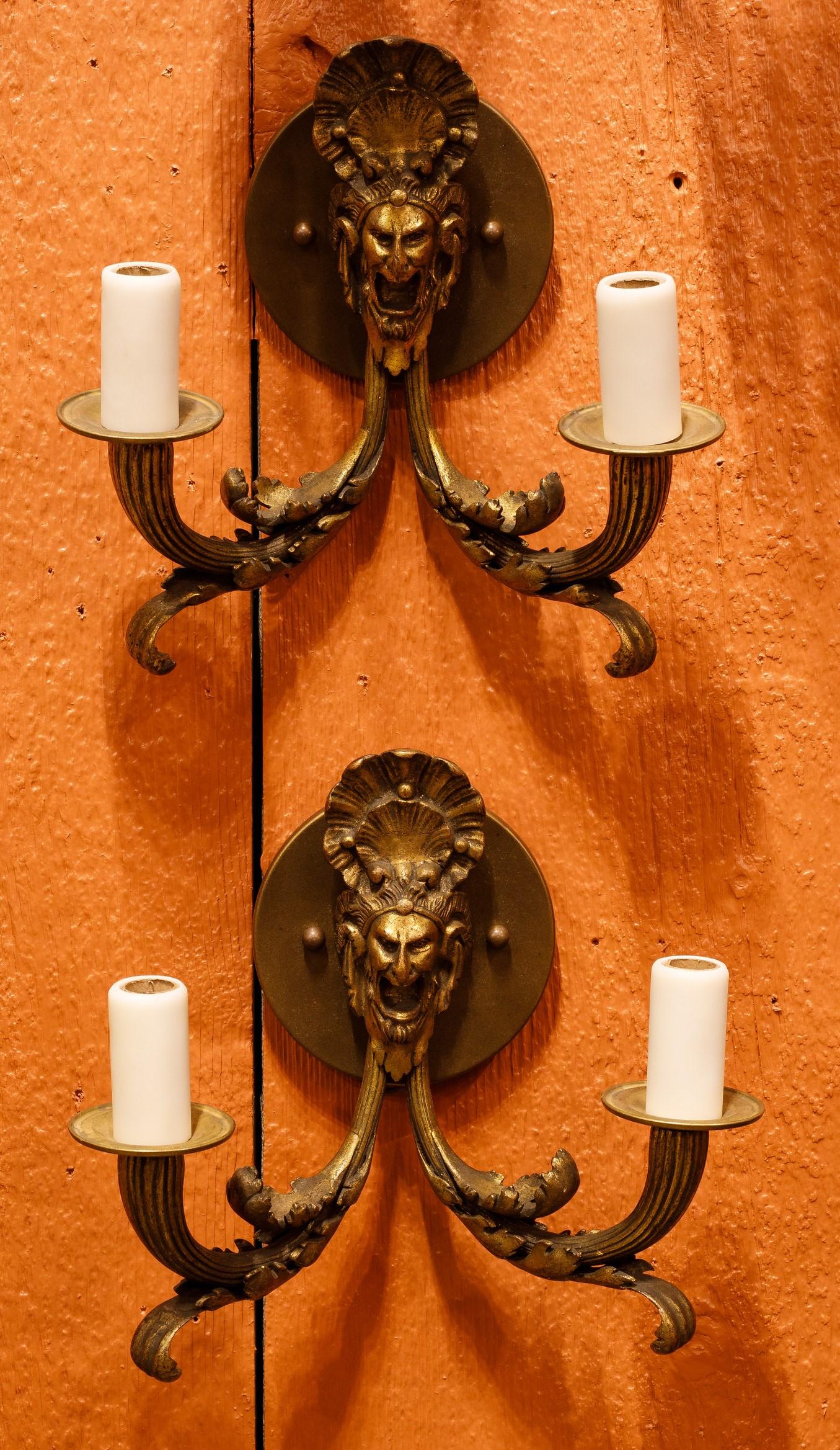 This pair of 2-arm antique bronze sconces has deep castings of fine quality  Their classic design is suitable for many rooms in a home.  The arms have beautiful castings of leaves and the center of the sconces have faces of Bacchus of Dyonysus.  The