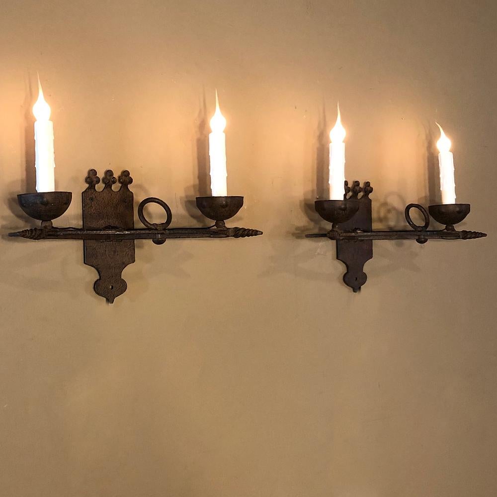 Pair of antique country French wrought iron wall sconces clearly display the talents of the blacksmith who forged them out of red-hot iron, and combine a shield motif with twisted rod, ring and bowl bobeches for a delightfully medeival look. Newly