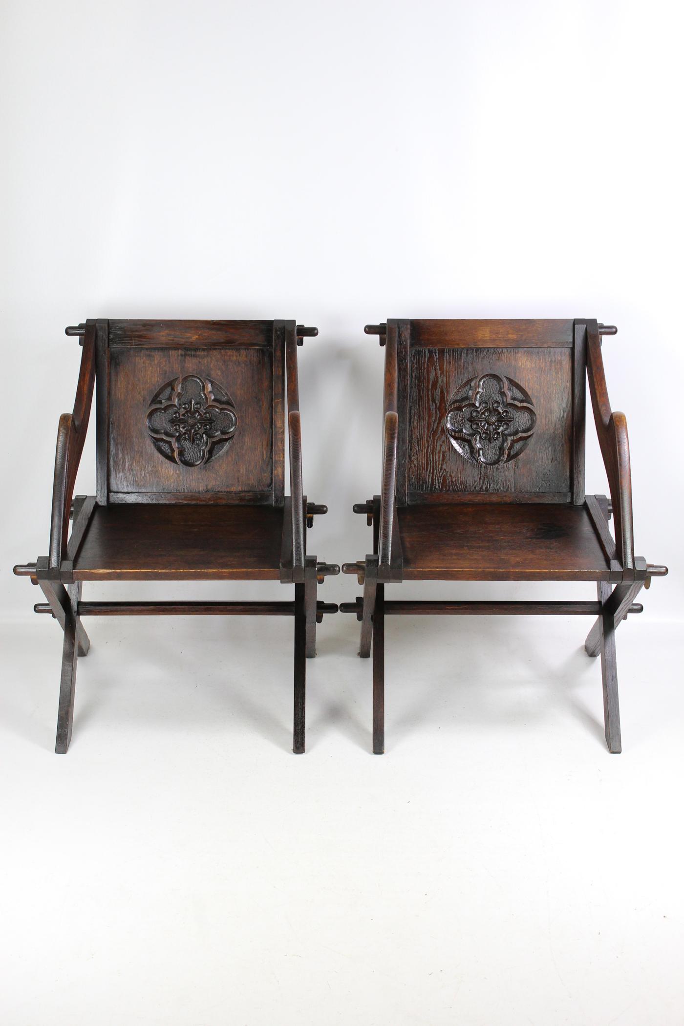 A good pair of antique early 20th century Arts & Crafts ‘Glastonbury’ armchairs dating from circa 1910. In solid oak with the distinctive shaped arms and raised on 'X' frame legs united by centre point stretcher, the backrests decorated with relief