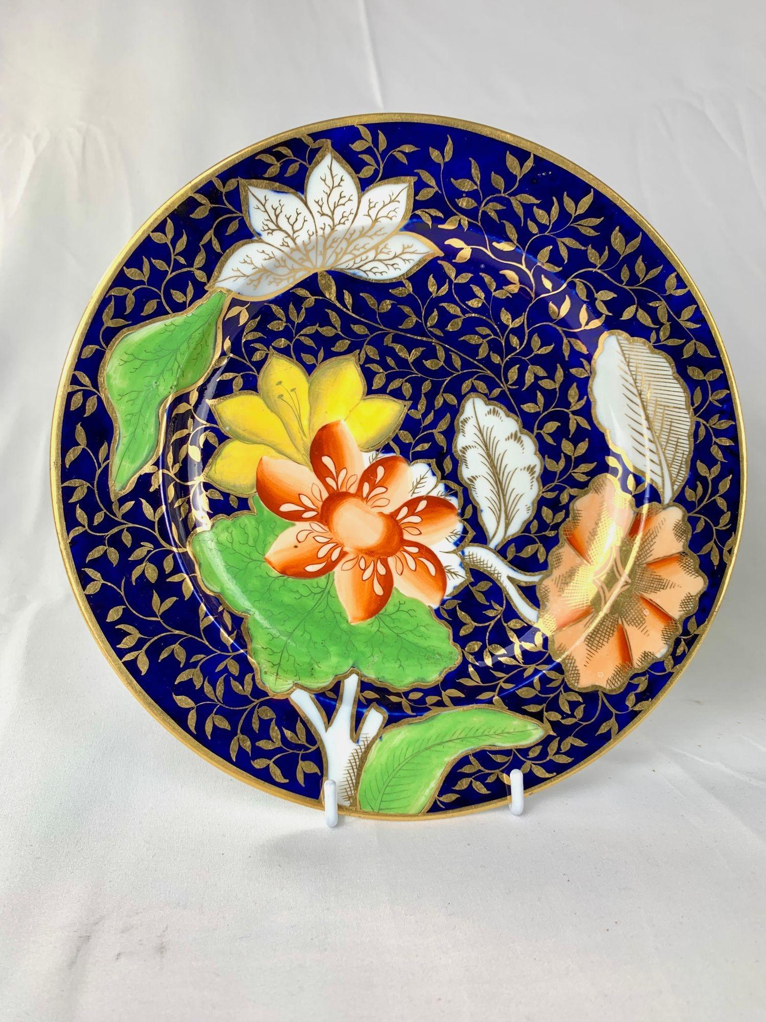 This vibrant pair of antique botanical porcelain plates was made by Coalport in Shropshire, England, circa 1810.
The standout feature is the elegant scrolling leaves rendered in gold against a luminous cobalt blue ground.
This rich combination of