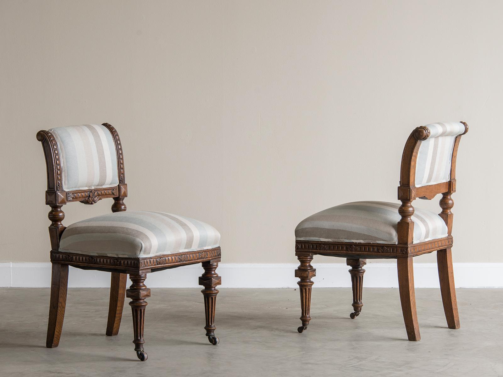 A pair of antique English William IV carved oak chairs circa 1875 with exceptional carving now freshly upholstered in a striped linen. Please notice that the front legs have wonderfully robust turned profiles and retain the original brass casters so