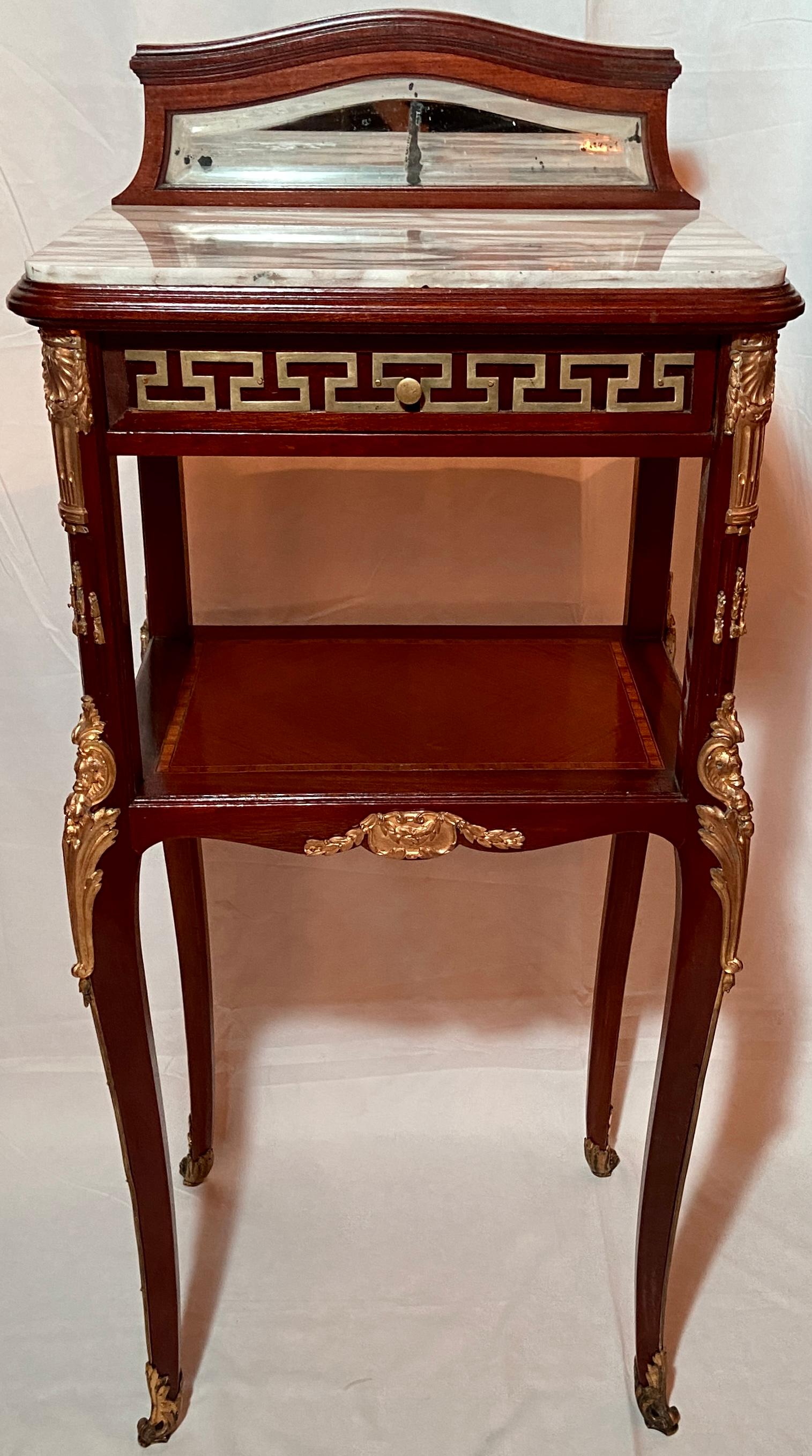 Pair Antique French marble top and bronze d' ore mounted inlaid mahogany nightstand tables, Circa 1890. Stunning pair with gold bronze details and beveled mirror backs.