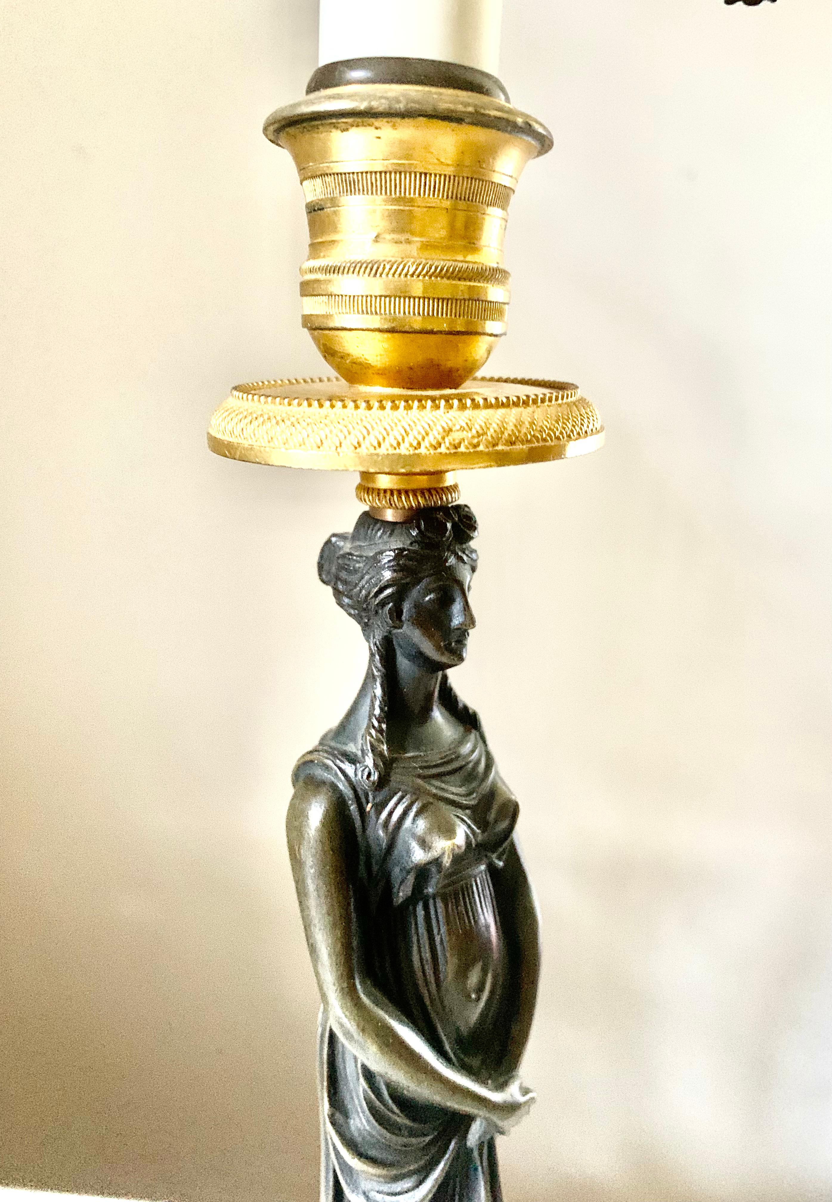 Classical Empire gilt and patinated bronze lamps depicting beautiful maidens in flowing Grecian garb, balancing fine gilt bronze candle holders on their heads and standing on dark grey cylindrical slate bases. Converted to electricity with two