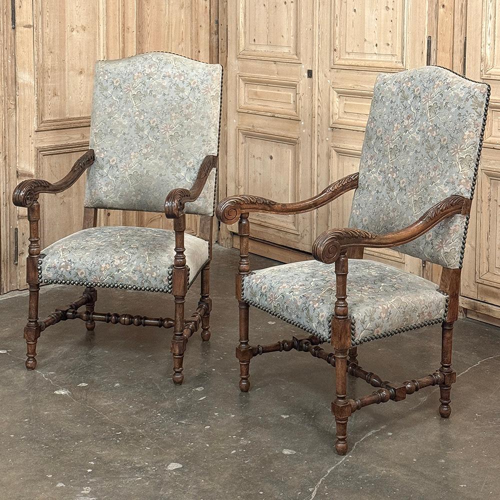 El par de sillones Luis XIV franceses antiguos se fabricó con roble macizo y tela fina y lujosa para crear un grupo de asientos majestuoso que ofrece tanta comodidad como estilo.  Los respaldos altos y arqueados y los generosos asientos están