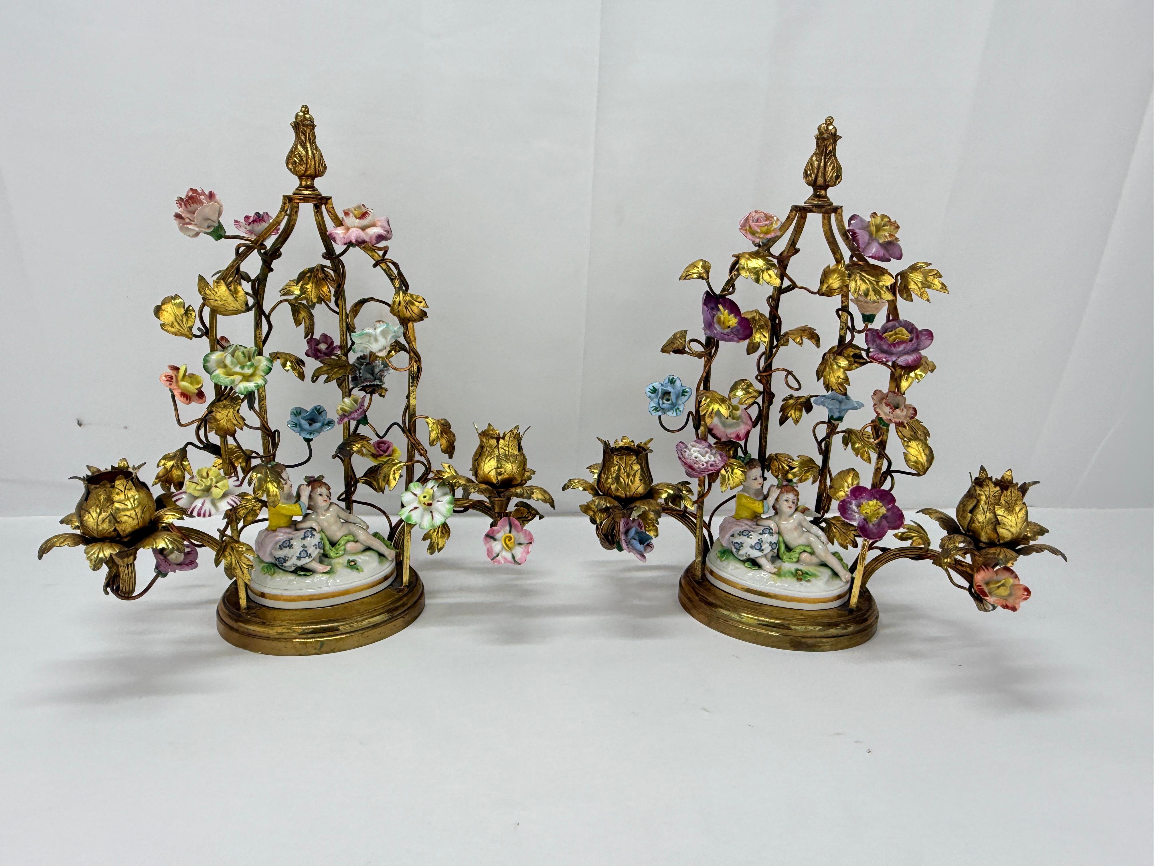 Este exquisito par de candelabros combina el bronce dorado de estilo rococó con la porcelana delicadamente pintada a mano. Cada candelabro presenta un marco ricamente adornado de volutas foliadas doradas y enredaderas trepadoras, intercaladas con
