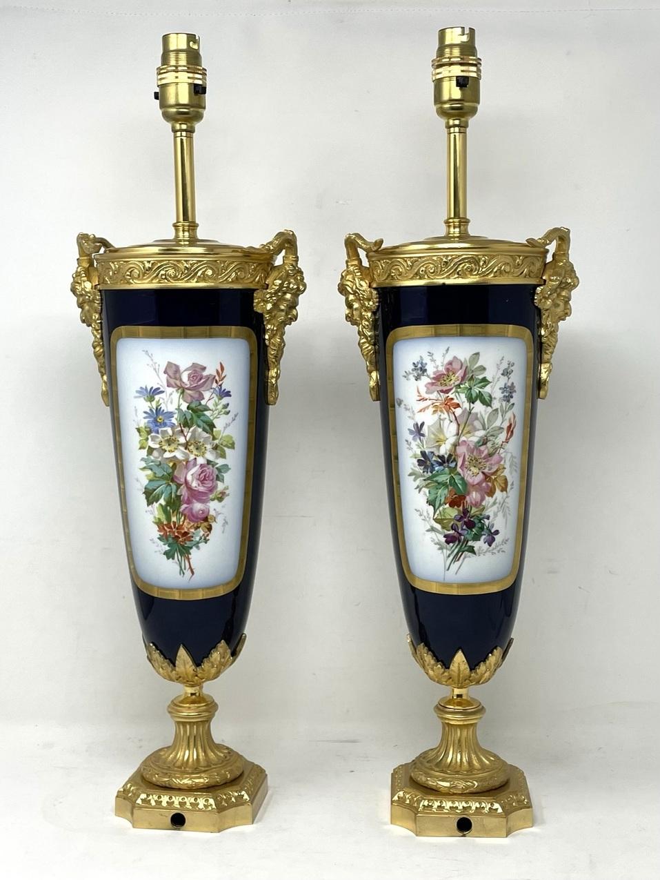 Stunning and imposing pair French Sevres soft paste porcelain and ormolu twin handle electric table lamps of traditional Urn form, and of good size proportions, raised on reeded dome shaped circular stepped bases with ornate canted corners.  

The