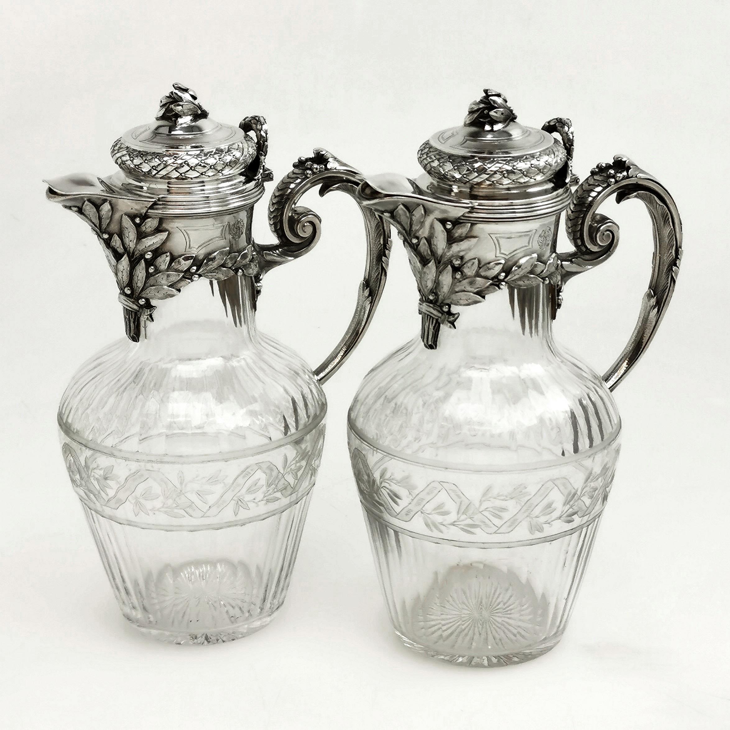A beautiful pair of antique solid silver and cut glass claret jugs. The silver mounts on the Jugs are embellished with ornate design elements including a bundle of chased leaves below the spouts and leaves on the finial. This leaf theme is continued