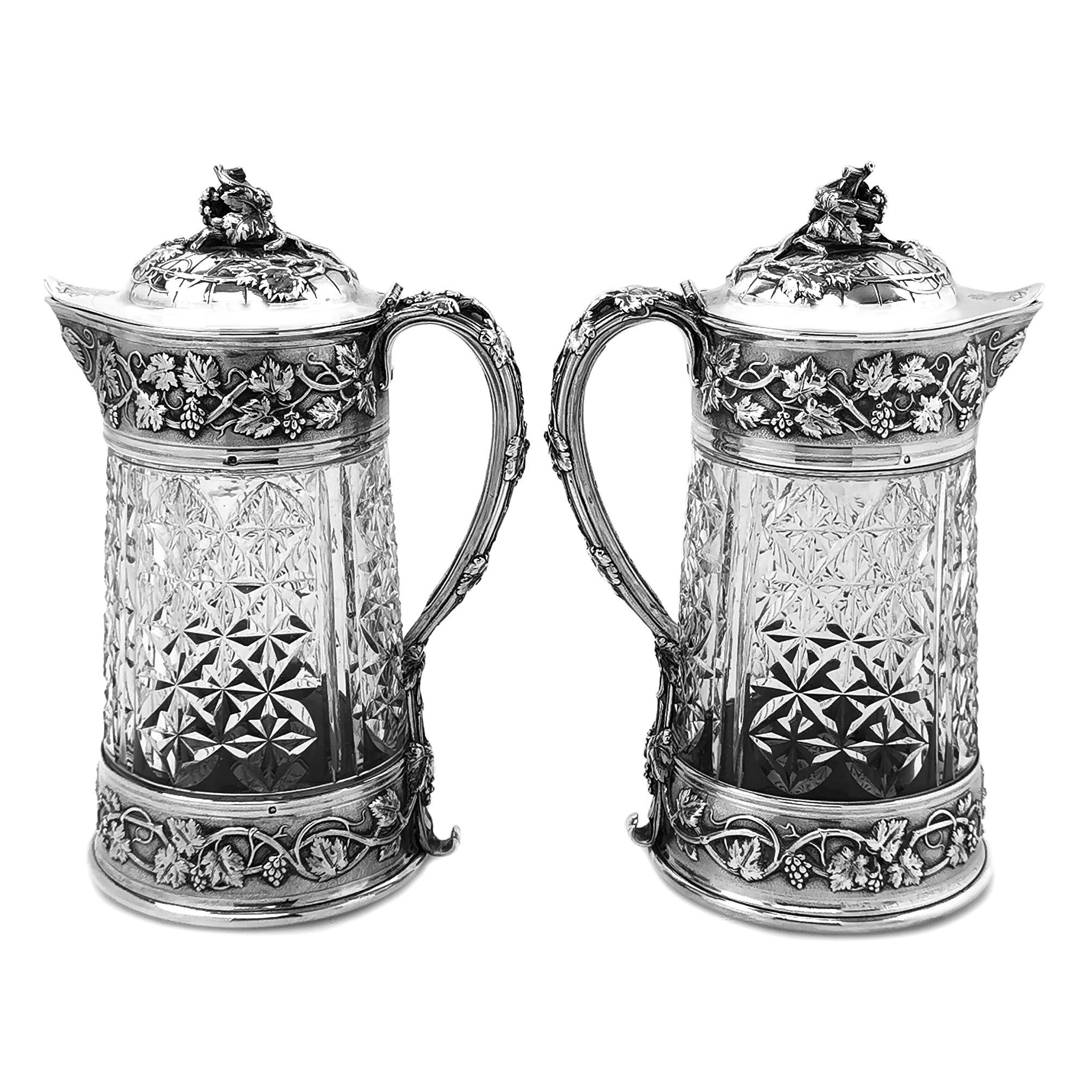 A magnificent pair of Antique French Silver and cut glass Claret Jugs. These 19th century Wine Jugs are of notably large size, and are embellished with an impressive chased grape vine design on the silver neck and base. The domed lid and elegantly