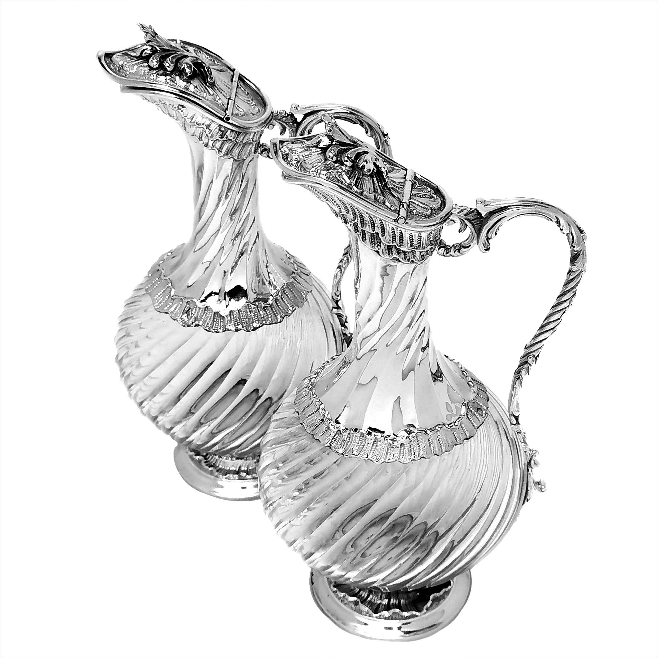 A pair of elegant antique silver mounted French liquor jugs with an subtle writhen fluted design on the clear glass body that is mirrored on the silver neck of the jug. The jug has chased patterned bands on the foot, body and neck. Similar to