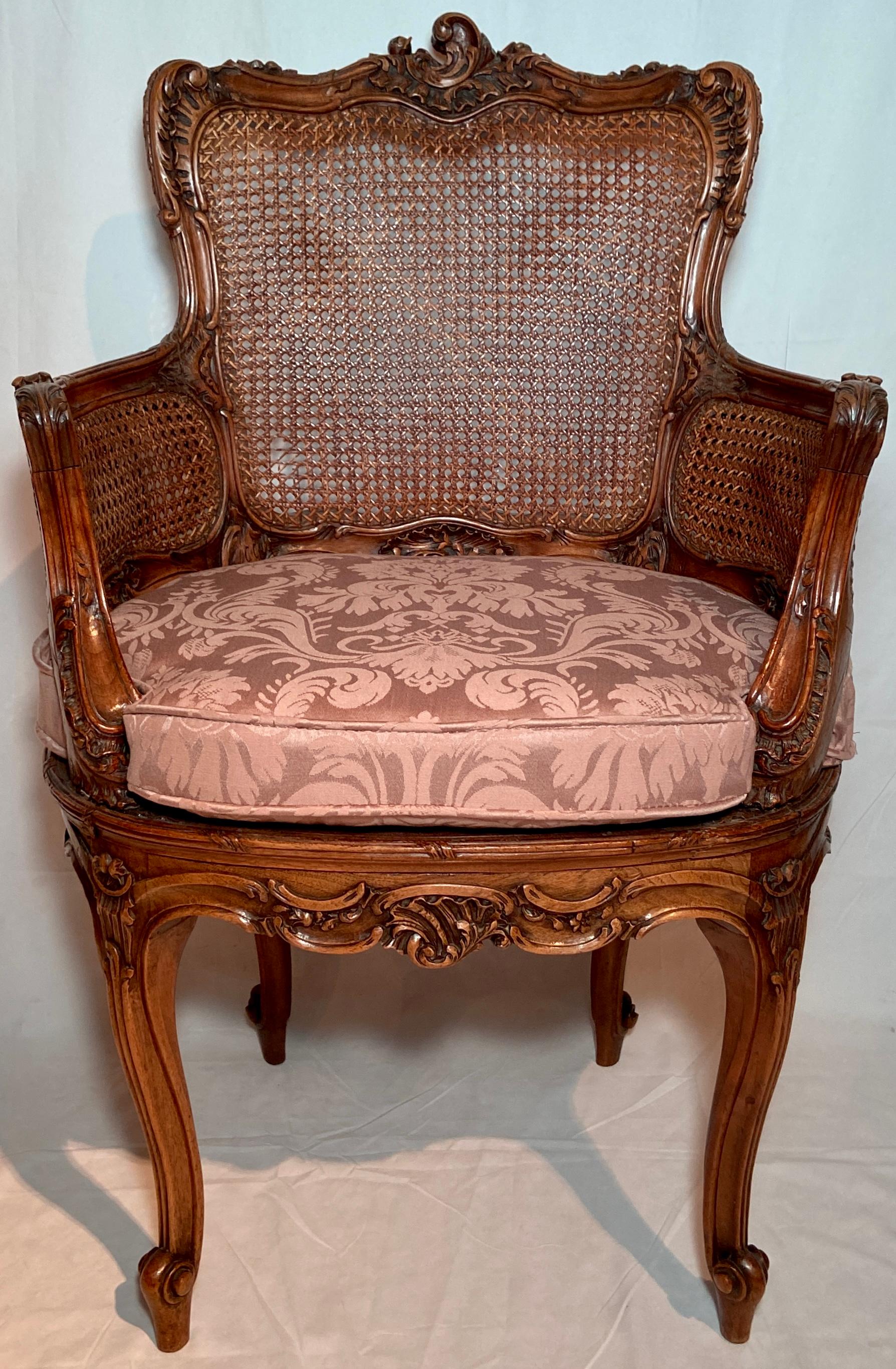 Pair antique French walnut and cane arm chairs with carved backs and pink silk upholstered cushions, circa 1890s.