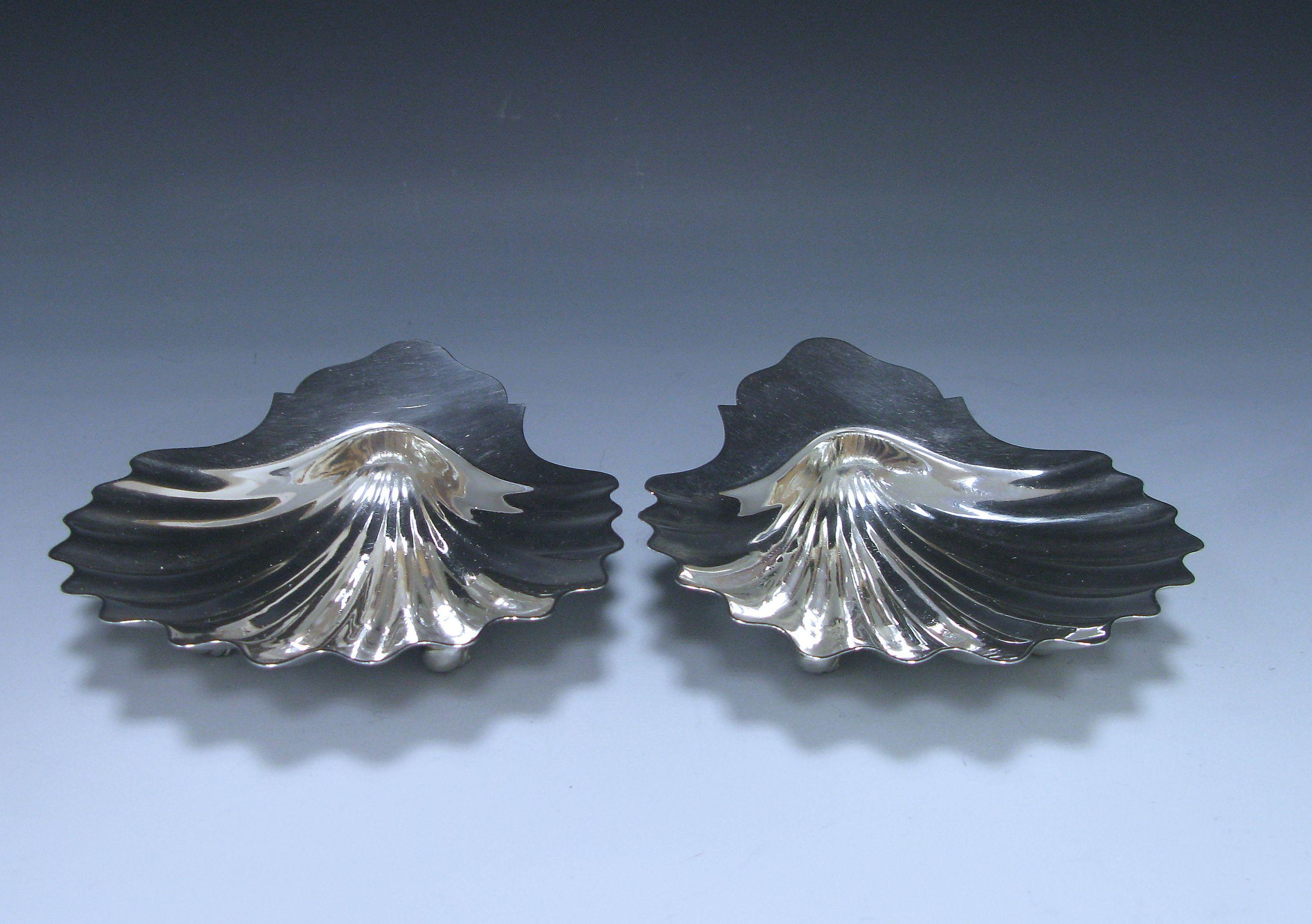 An elegant pair of antique George III sterling silver butter shells in the traditional shell form. The dishes are supported by three nautilus feet, combined weight 6.6 troy oz.