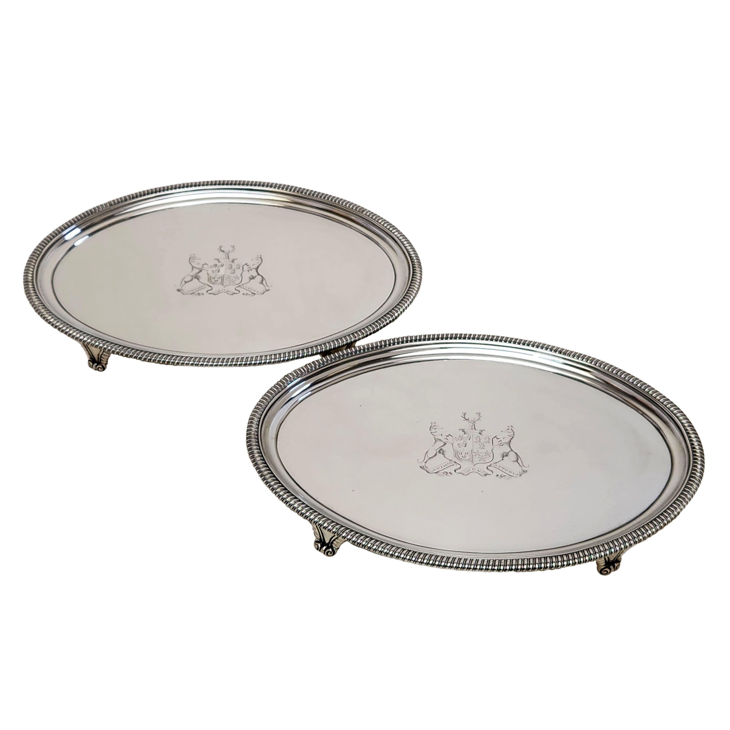 A pair of elegant George III Oval Silver Salvers with classic gadroon borders. Each Salver has an impressive armorial engraved in the centre. Each Georgian Salver Stands on four gadroon patterned feet.

Made in London, England in1806 by John