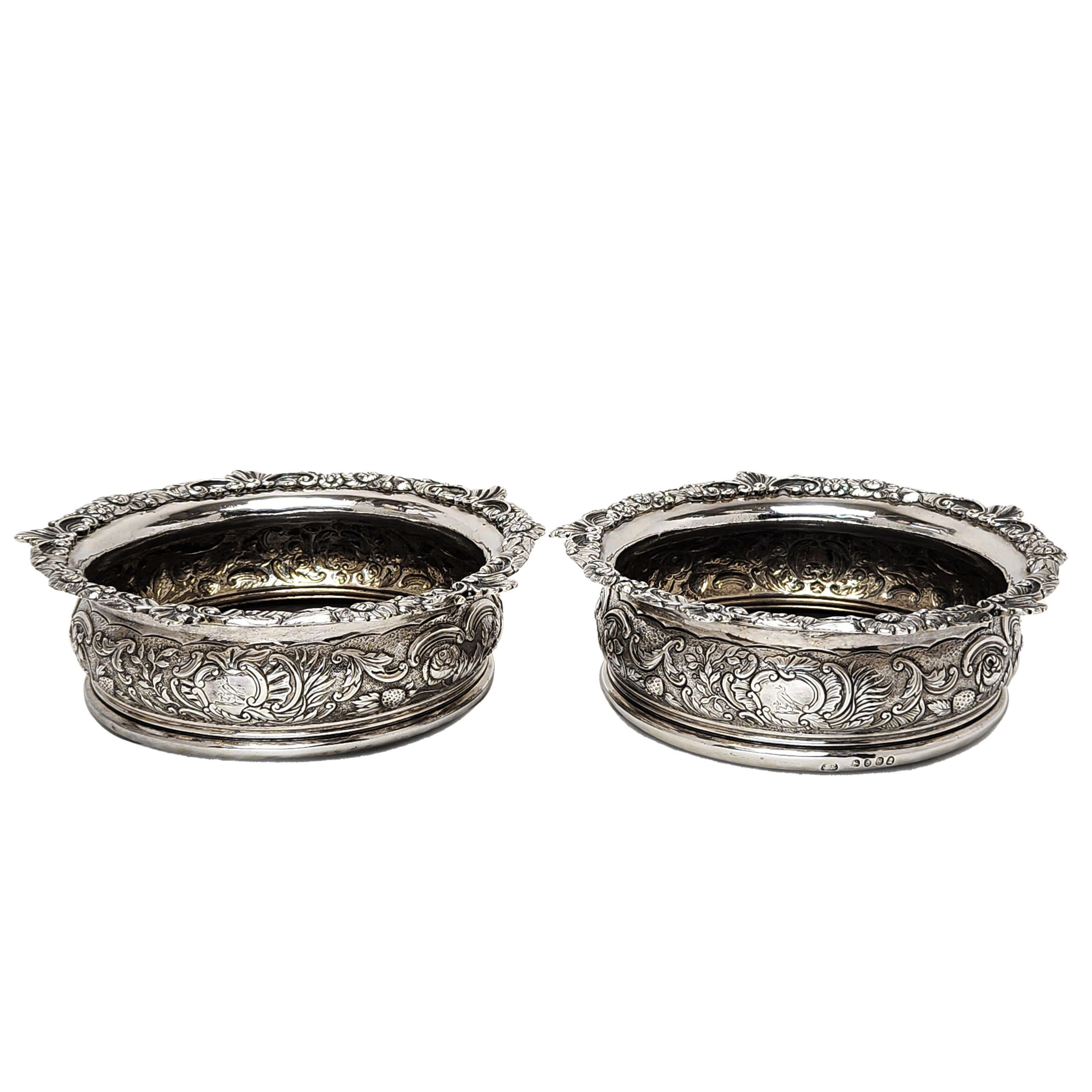 A pair of elegant Antique George III Silver Wine Coasters decorated with a lovely chased design featuring scrolls, foliate and floral elements and fruit. Each Silver Coaster has a pair of cartouches and one on each has a small bird crest engraved.