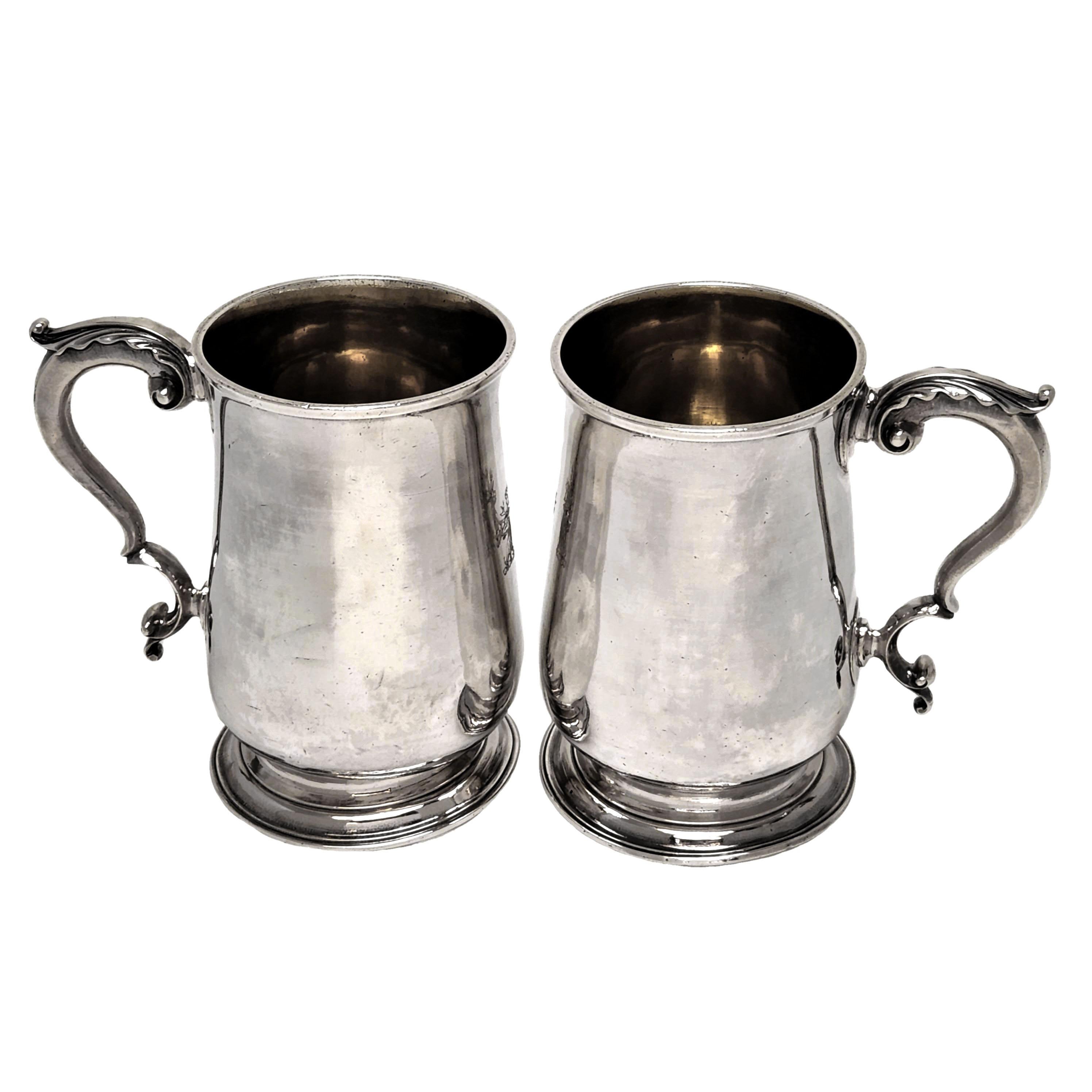 A pair of excellent Antique George III Solid Silver Pint Mugs in a classic Georgian style. The Tankards each stand on a spread pedestal foot and each has a gilded interior. Both Mugs have a small crest engraved opposite the handle. These Mugs have a
