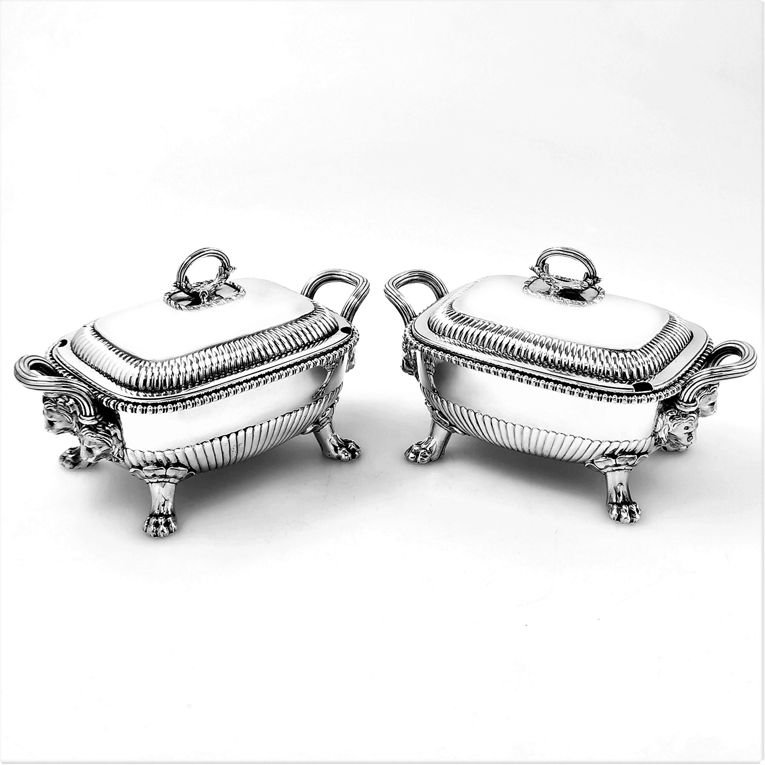 A pair of antique George III solid Silver Sauce Tureens featuring a classic fluted design on the lid and base. The Body of each Tureen features a pair of impressive handles each showing a pair of lion heads, and each tureen stands on four claw feet.
