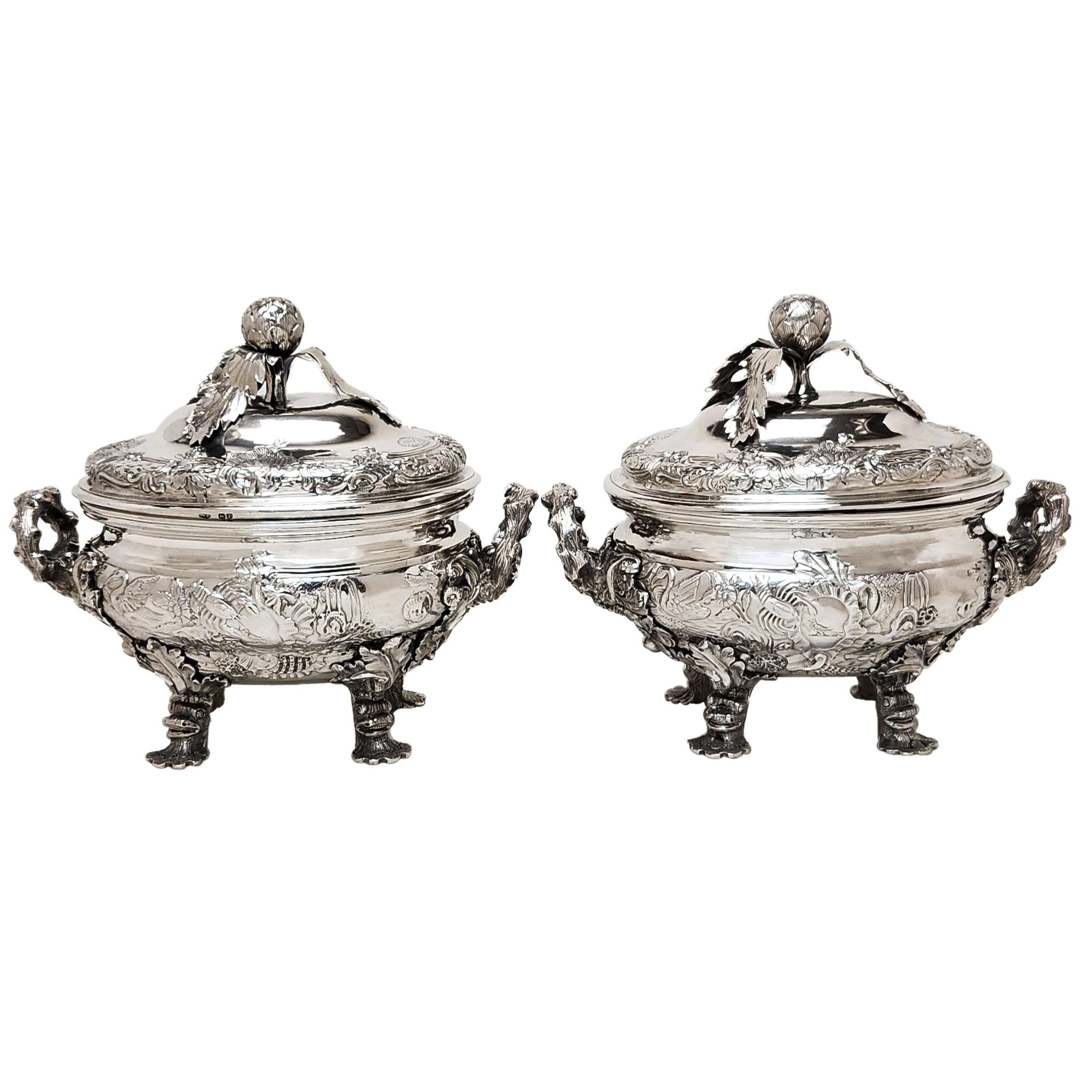 A pair of magnificent Antique George III Sterling Silver Sauce Tureens with ornate Rococo style chasing embellishing the body and lid of the Tureens. The Silver Tureens stand on 4 opulent feel supporting the body which features an intricate chased