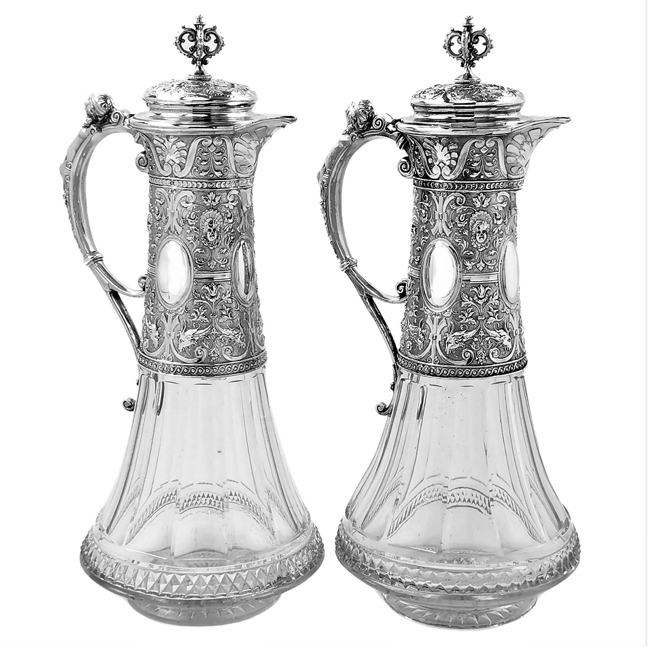 A pair of beautiful Antique German solid Silver mounted Cut Glass Claret Jugs. The Wine Jugs have tapered bases decorated with elegant cut glass patterns. The Wine Jugs have tall sterling Silver necks, with silver lids and curved handles. The Necks
