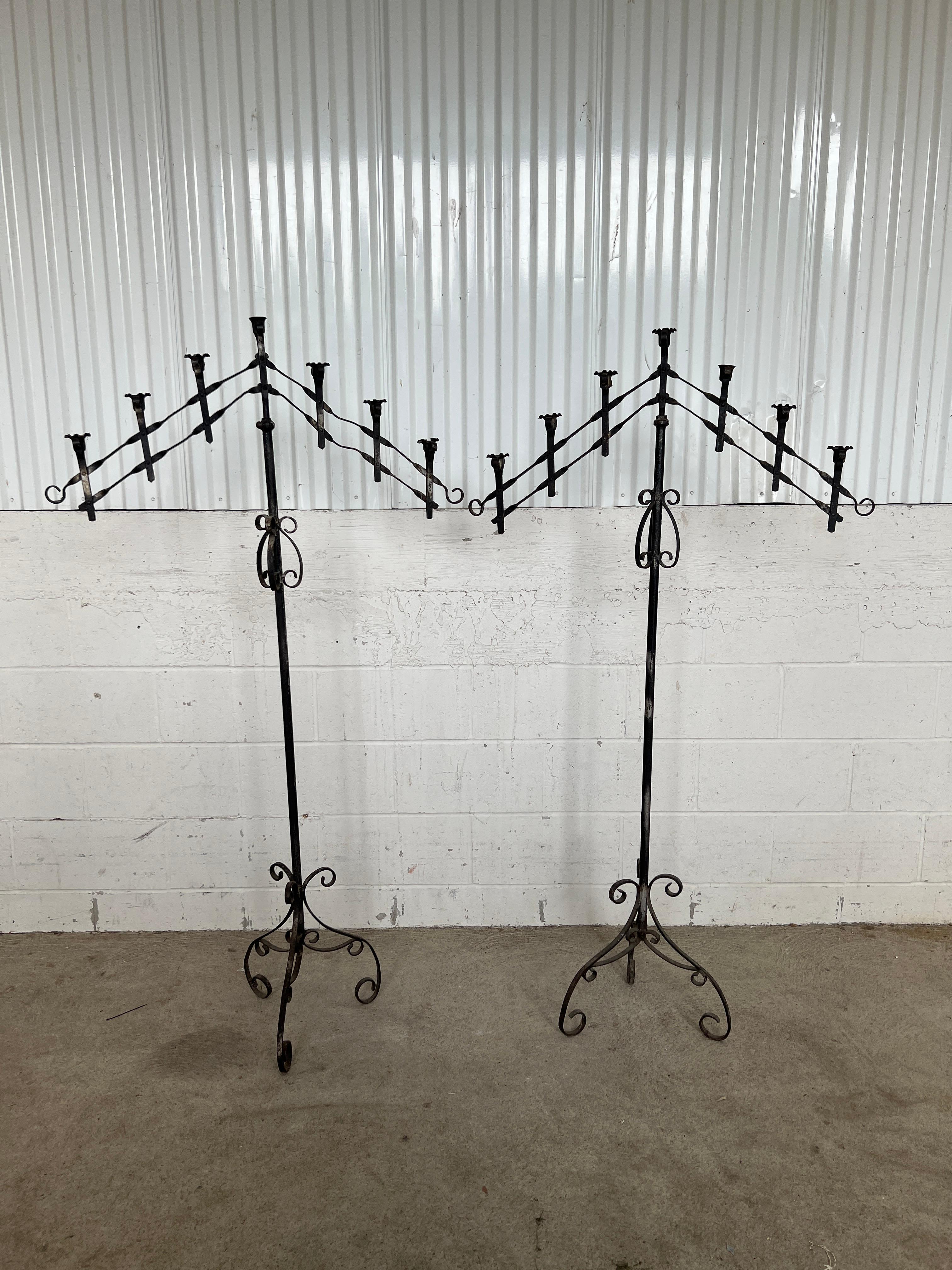 Likely Spanish in origin, circa 1920. 

A pair of wrought iron floor standing candelabra. Each having 7 shaped candle holders that are adjustable in width from 14.5