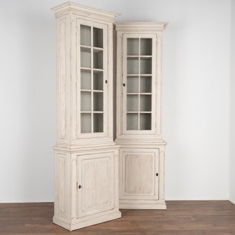 Pair, tall narrow gustavian column cabinets built in two sections each.
Traditional carving along front and side panels, beaded trim under crown.
Later applied professional white painted layered finish, slightly distressed to compliment the age
