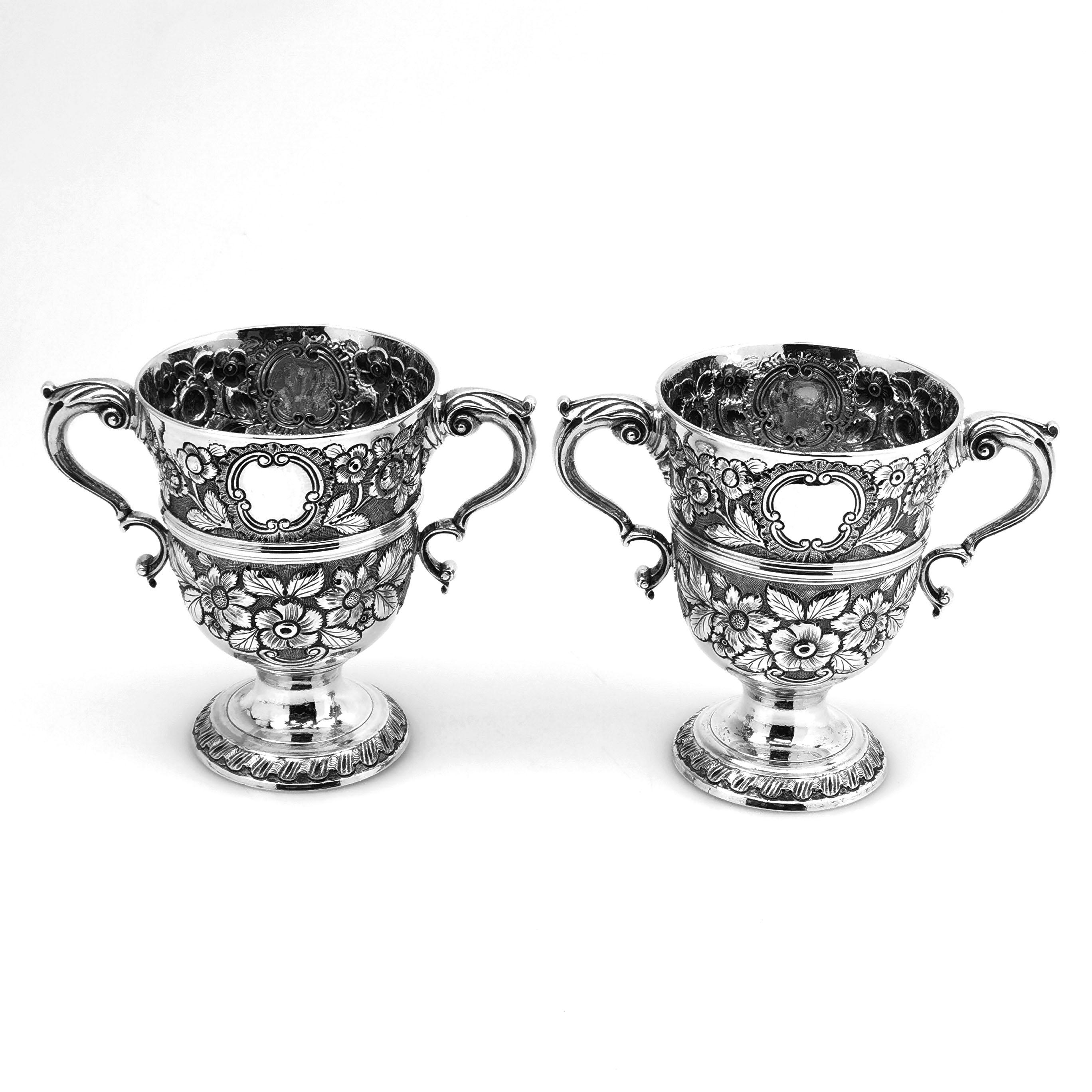 A lovely paid of Antique Irish Silver Cups. These 18th century Cups are embellished with ornate floral chased designs and each cup has a pair of shaped cartouches. Each Cup has a crest engraved in one of the cartouches while the other is plain