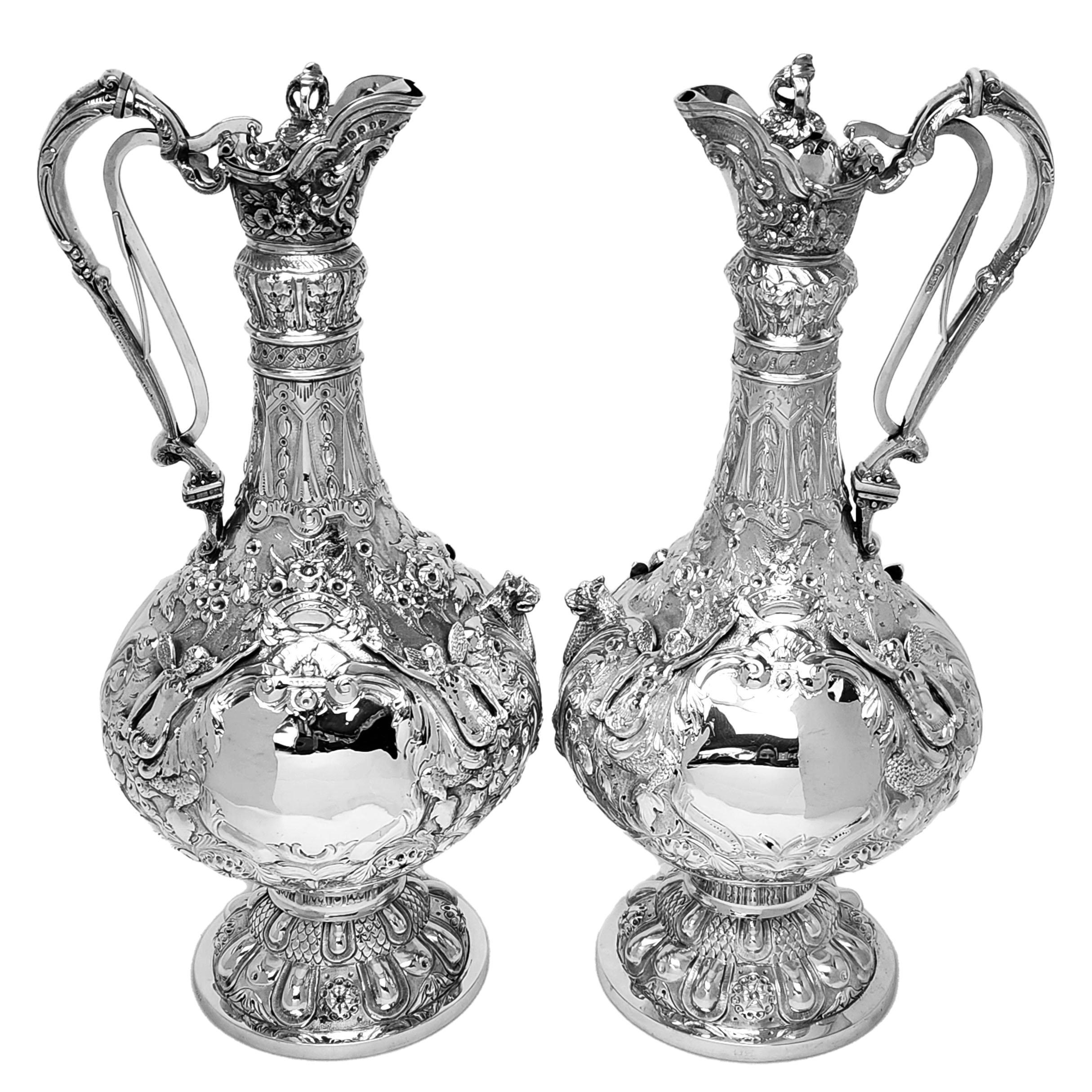 An impressive pair of Antique Irish sterling silver Claret jugs in a traditional Armada Style. This Pair of Armada Wine Ewers feature rich and ornate chased and applied detailing over the entire body of the jug. These chased decorative elements
