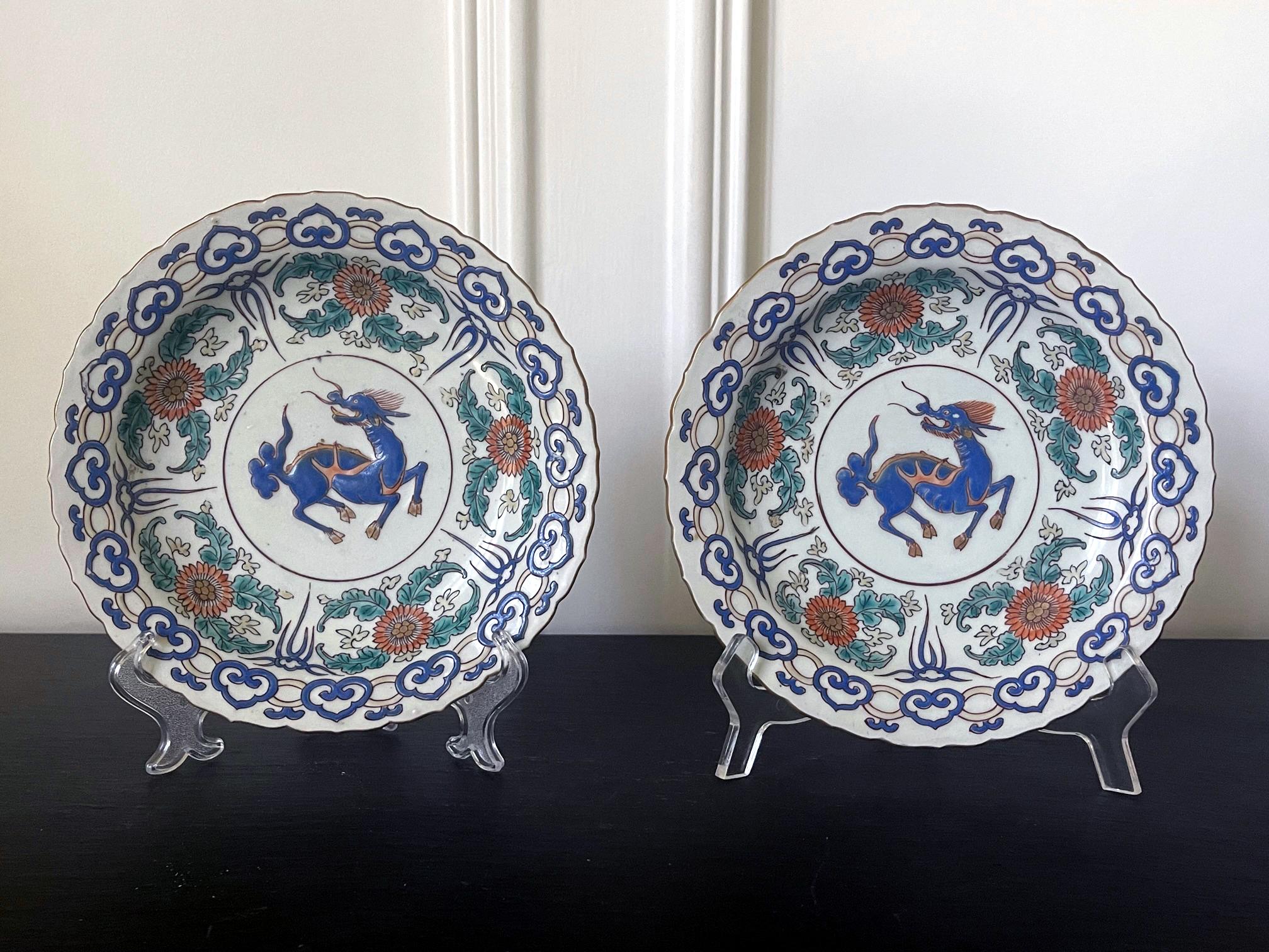 A pair of Japanese decorative ceramic plates, made in Arita for export market circa 17-18th century. The cabinet-display dishes feature lotus-petal gilt rim and a lavish tricolor enemal glaze decoration on a grey-white background. The center