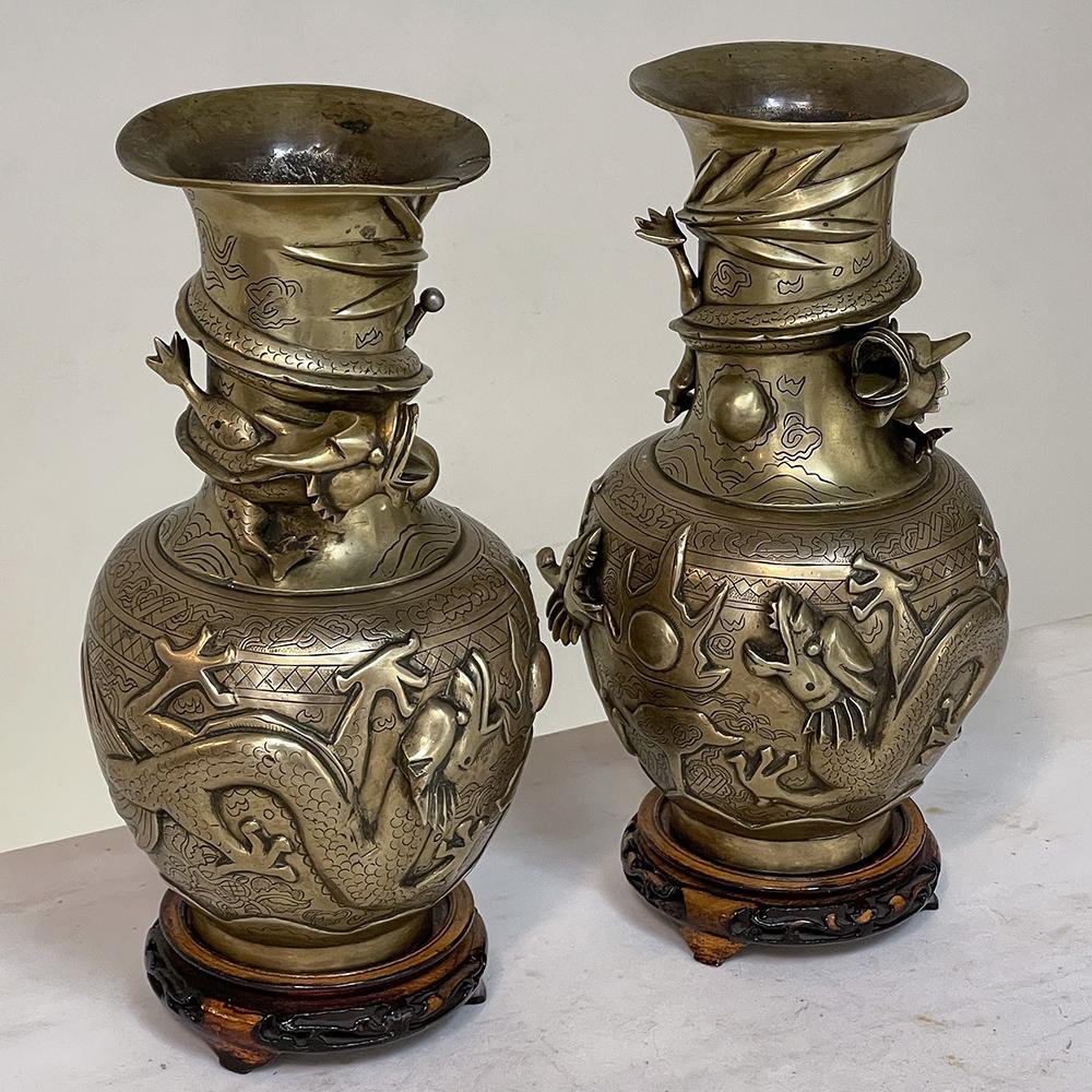 Pair Antique Japanese bronze vases on wood stands are ideal for adding beautiful symmetry with the magic of the Orient! Encircled with three-dimensional dragons on the upper portion, with full relief dragons encircling on the body below, each