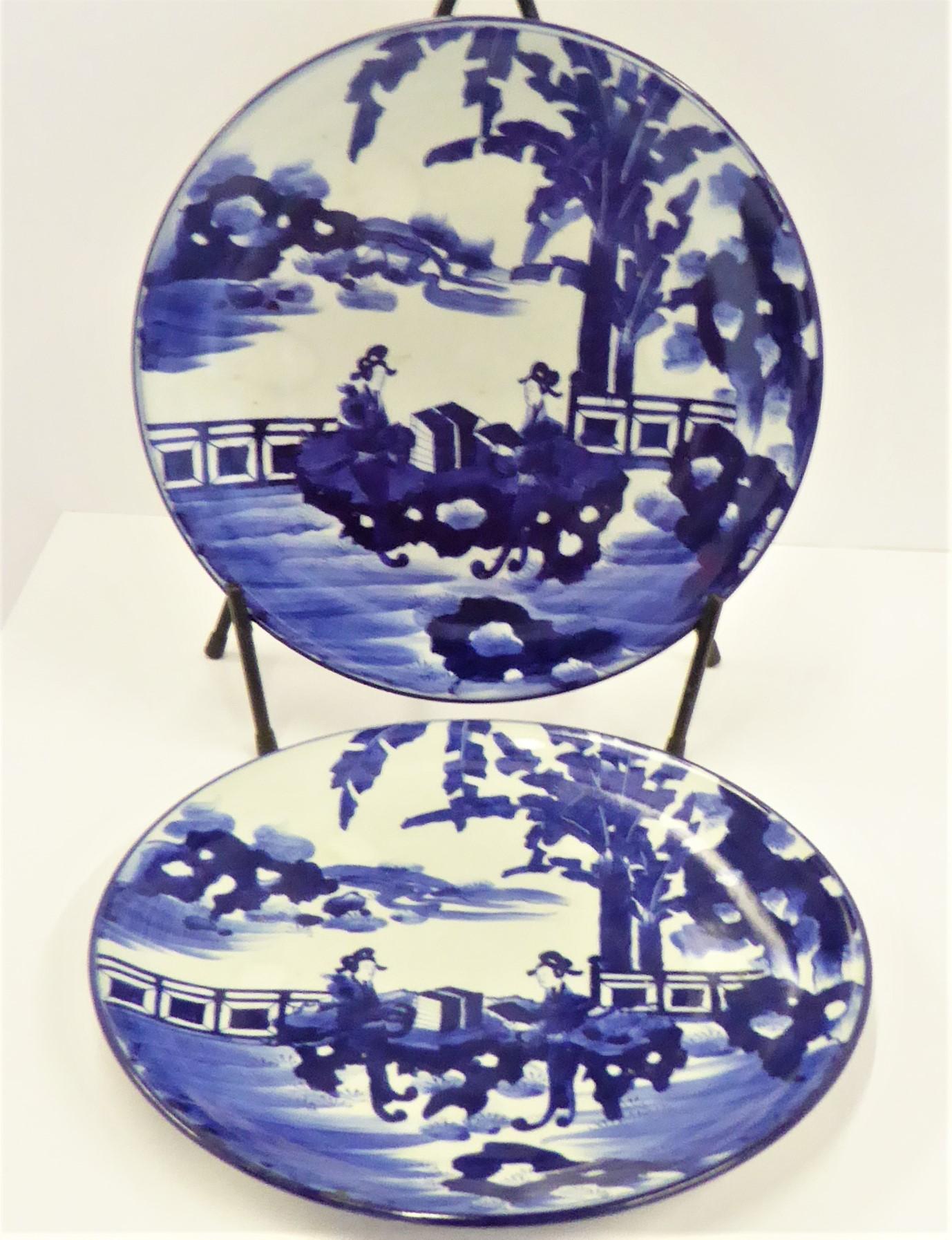 Beautiful pair of Meiji Period blue and white Japanese Imari Chargers depicting two Japanese Courtesans reading poetry by a lake in a serene setting framed by banana palms or trees on one side of background. Matching in design, both platters have