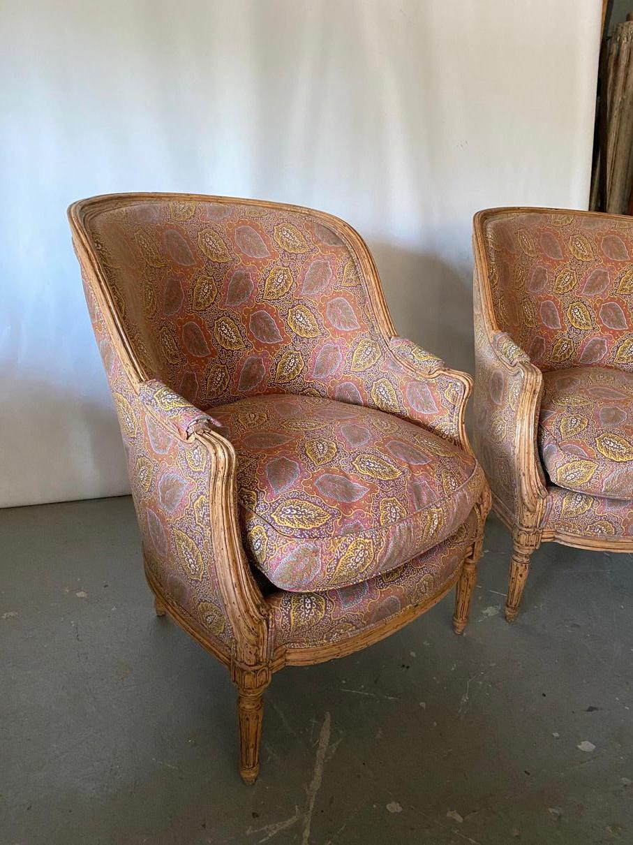 Generously and well proportioned antique down filled fruitwood barrel back Louis XVI style bergère armchairs. Wonderfully comfortable. Upholstery shows wear. Currently upholstered in a paisley fabric, with a down filled loose cushion.