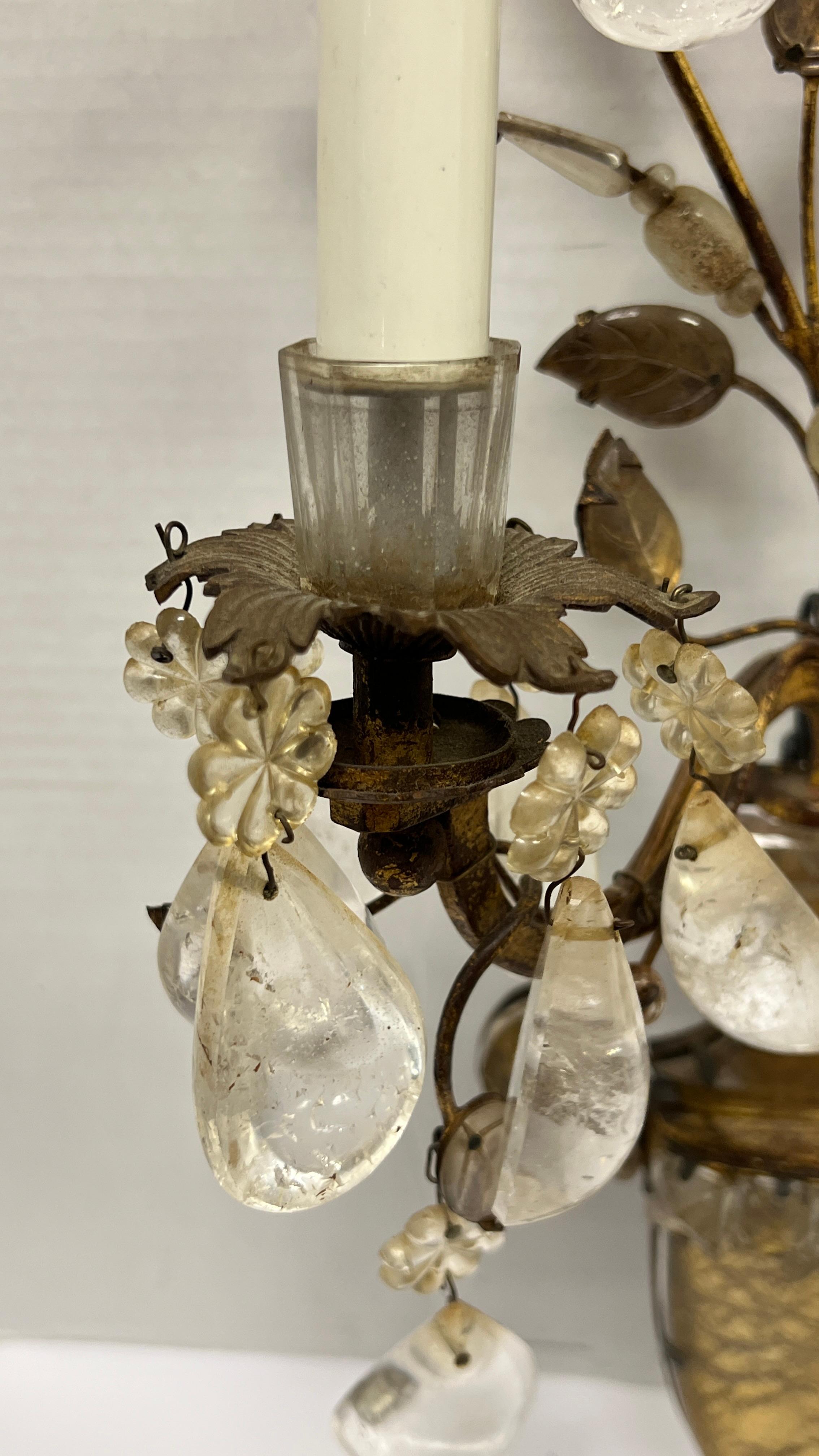 Our pair of antique French wall lights, attributed to Maison Bagues, are crafted from gilt metal, crystal and rock crystal.  They have an urn form with flower petal and leaf designs and pair of electrified candles with their original ceramic