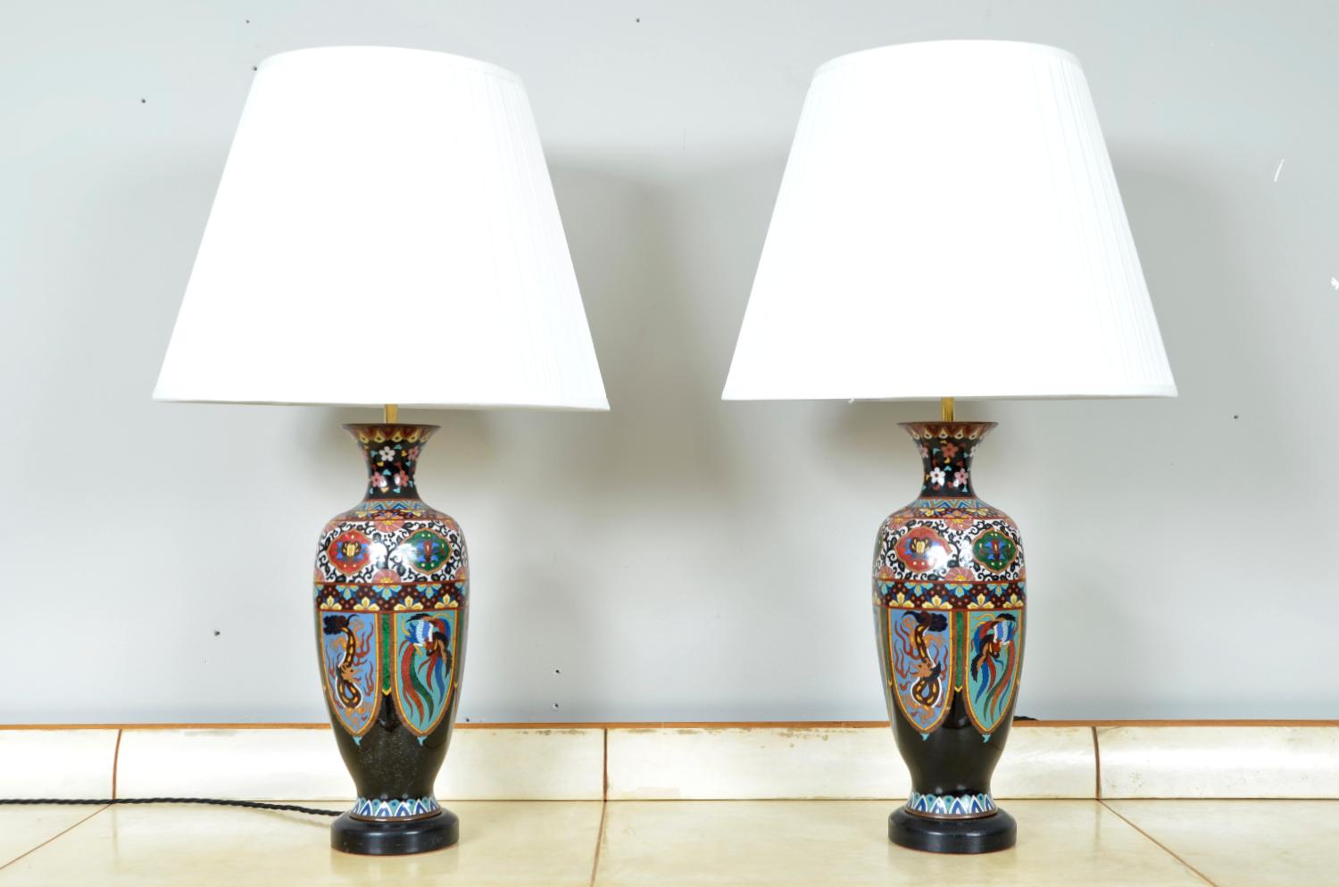 A large and exquisite pair of matching Japanese Cloisonné table lamps on ebonised bases, profusely decorated with polychrome enamelled mythical beasts inspired by dragons and birds that add a touch of mystique to the vases. This pair of Japanese