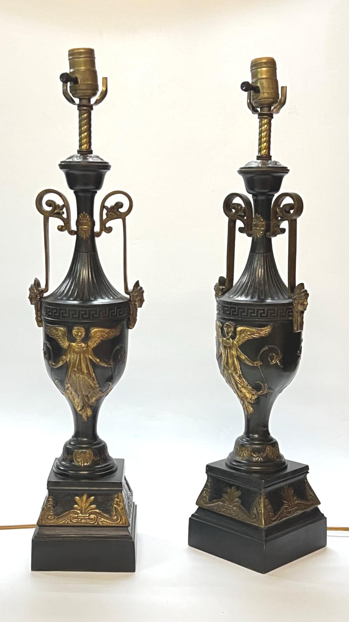 Pair of antique bronze table lamps in the form of neoclassical vases with the figures of winged goddesses, masks, and Greek key motifs.  With sockets and wiring, ready for use.