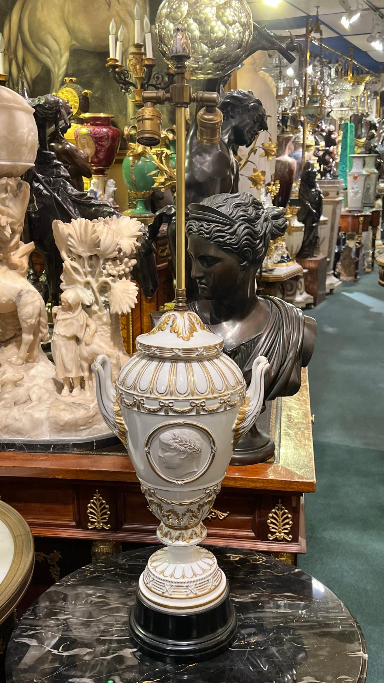 Pair of antique white glazed porcelain vases in the neoclassical empire style mounted as table lamps with tall brass standard with gilt porcelain finials and mounted on ebonized wooden pedestals with circular on/off switches.  Featuring the profiles