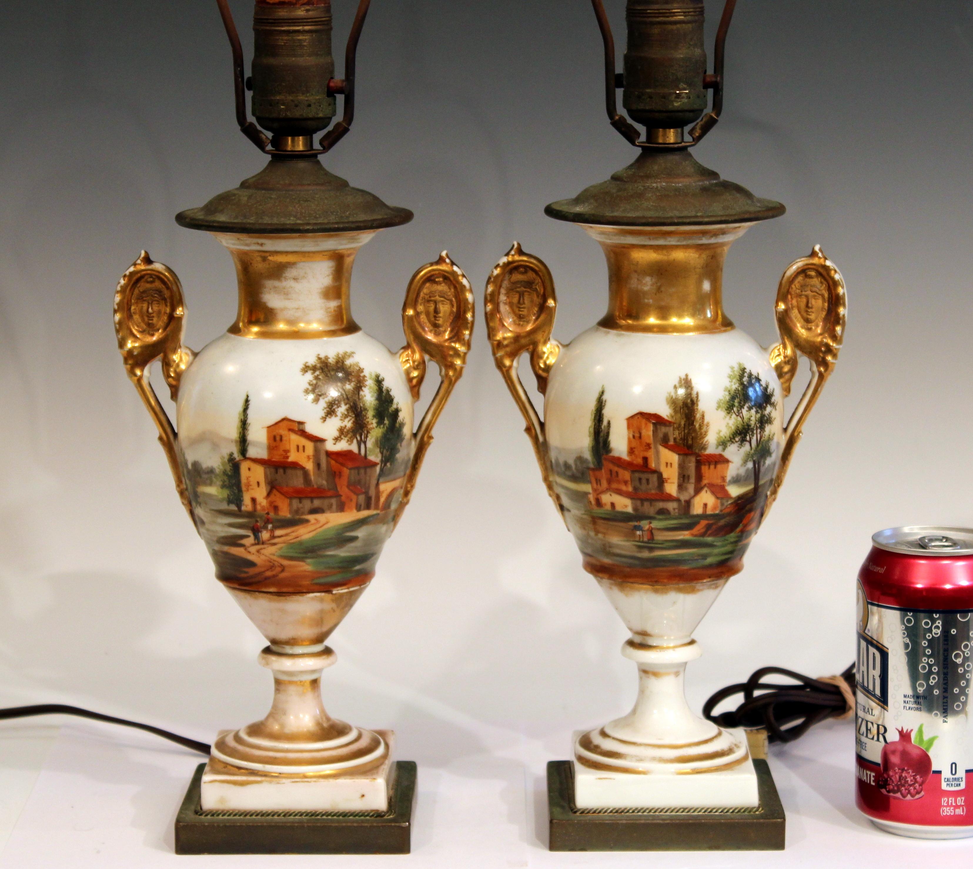 Pair antique Paris porcelain vases mounted as lamps with scenes of the French countryside, circa early mid-19th century. Four different hand painted scenes with beautiful two-tone gilding and face details on handles. 20
