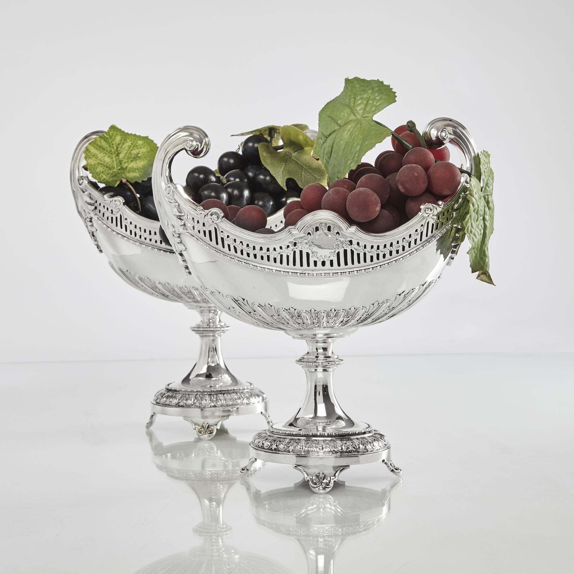Pair of heavy quality and elegant fruit stands with oval dishes and pedestal bases. With cast scroll and acanthus leaf handles, and decorative fluting to the bottom half, this pair of Edwardian silver bowls are hand-pierced and hand-engraved. They