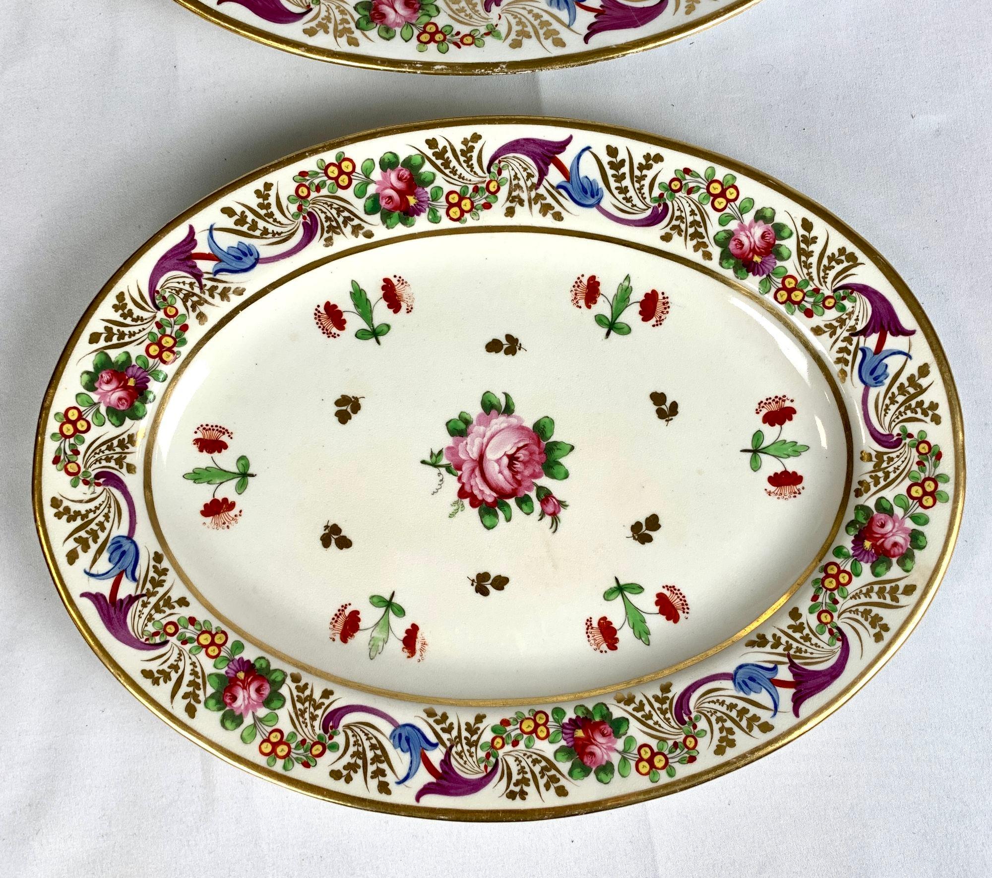 This pair of brightly colored oval dishes are each decorated in the center with an exquisite rose hand painted in pink with green leaves. Around it are six pairs of smaller red flowers, also shown with their green leaves. The lively borders are
