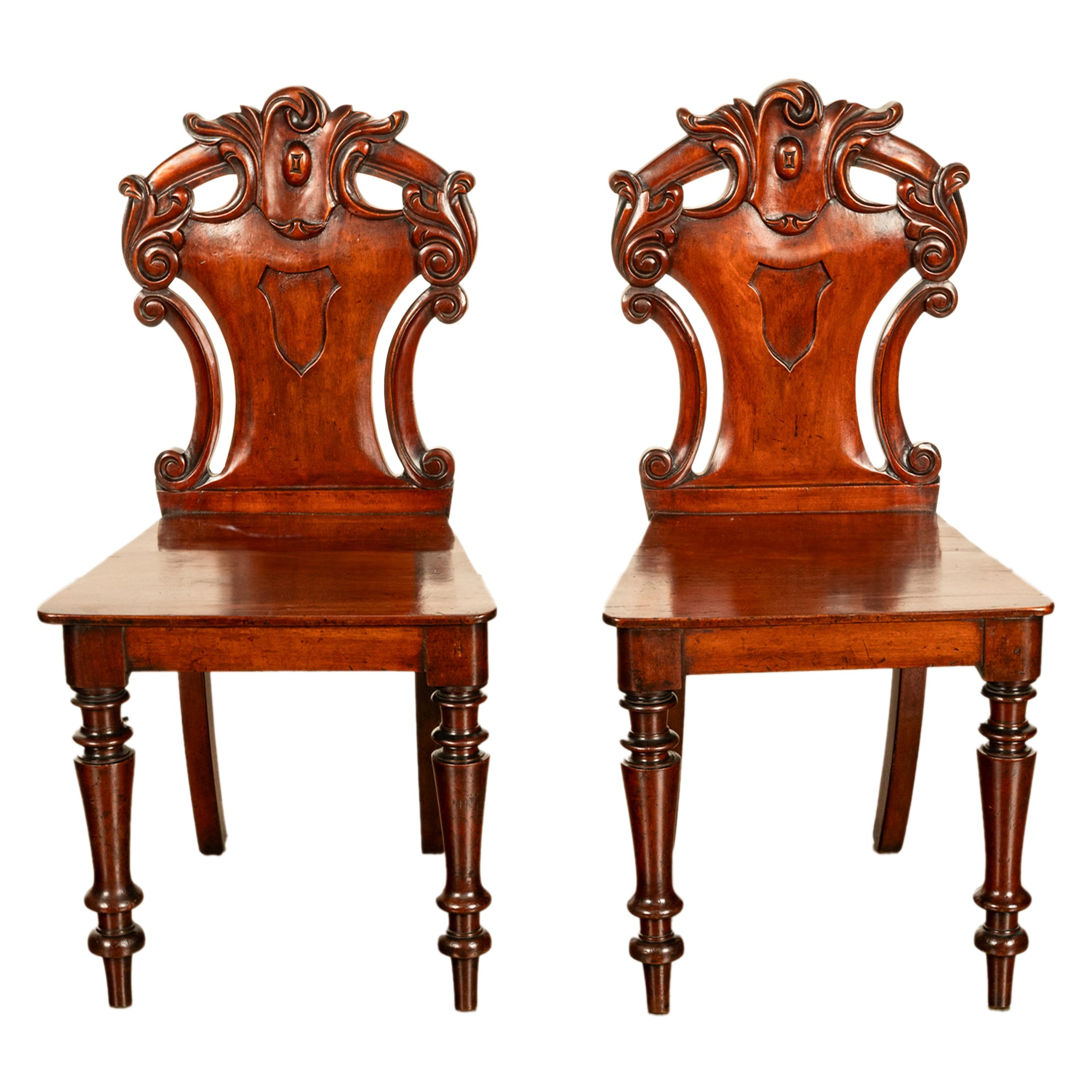 A good pair of antique carved mahogany Georgian Regency country house hall chairs, circa 1825.
The chairs are made of the finest solid mahogany, the backs are very well carved with rococo scrolls and each chair with having a shield carved in relief.