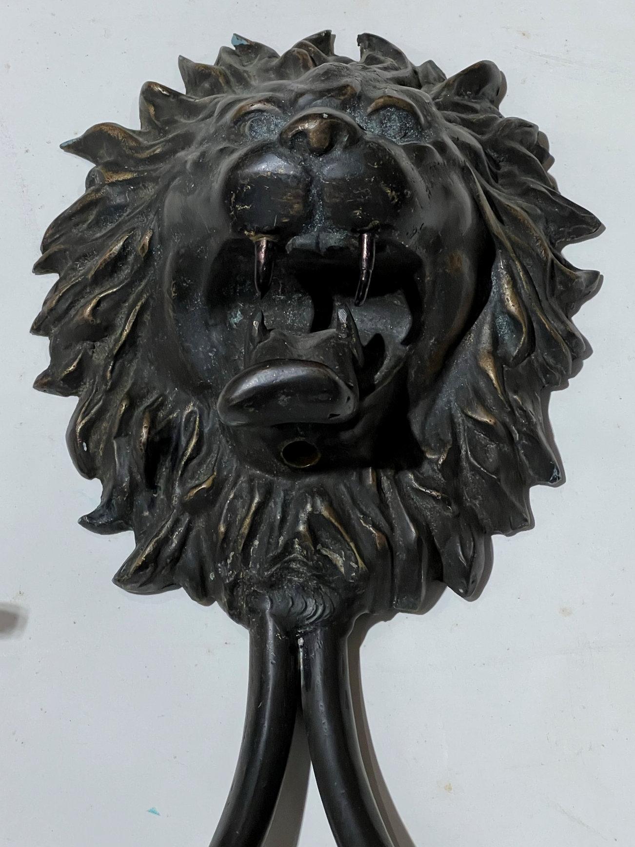 Pair of patinated bronze wall lights in the English Regency style with roaring lion masks and two electrified candle arms.  With modern sockets accommodating candelabra size bulbs.