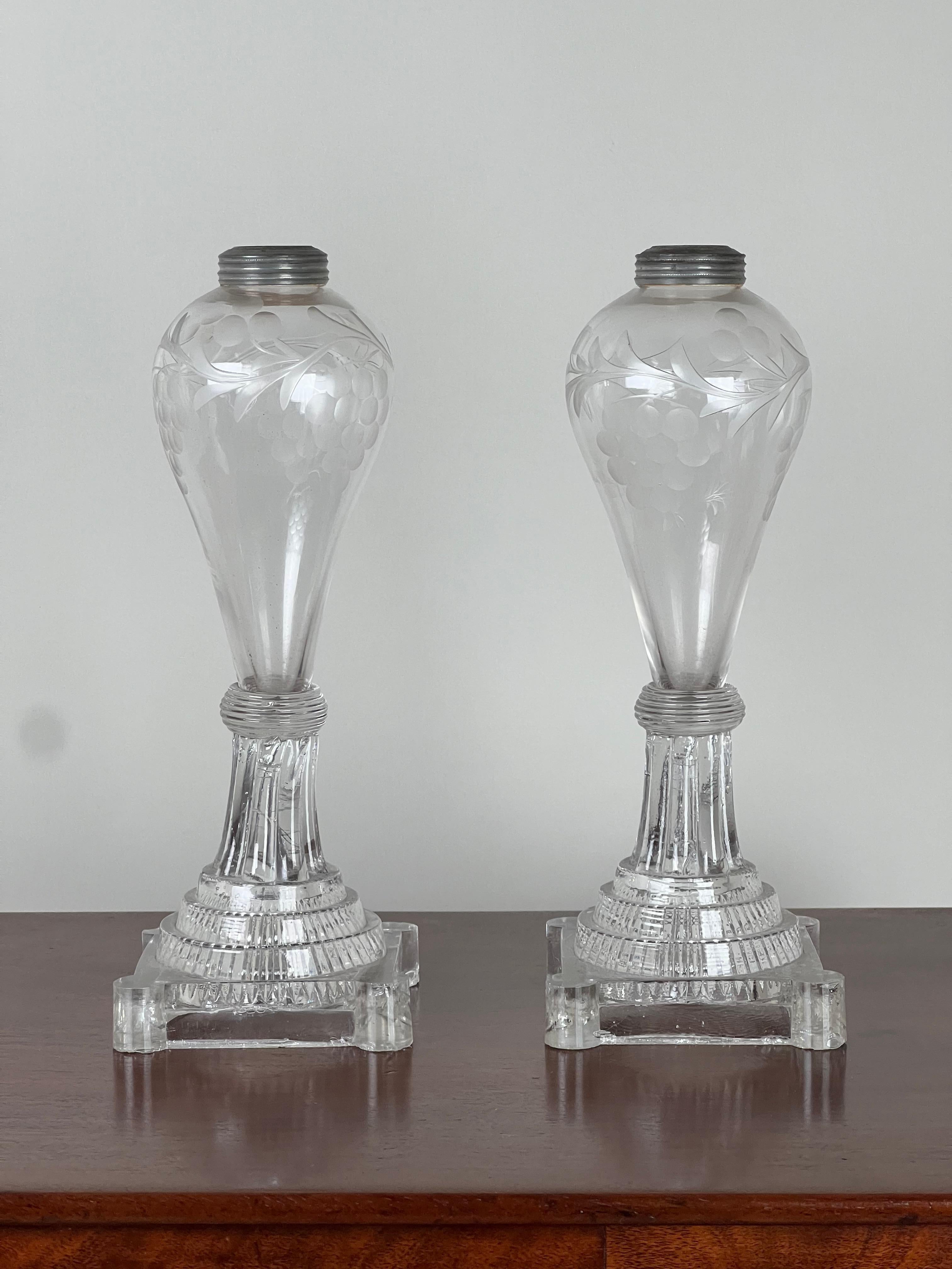 This elegant pair of early 19th-century Sandwich Glass whale oil lamps is a striking example of American craftsmanship from the 1820s. The lamps feature a delicate etched floral design, skillfully applied to the glass, with graceful vines and