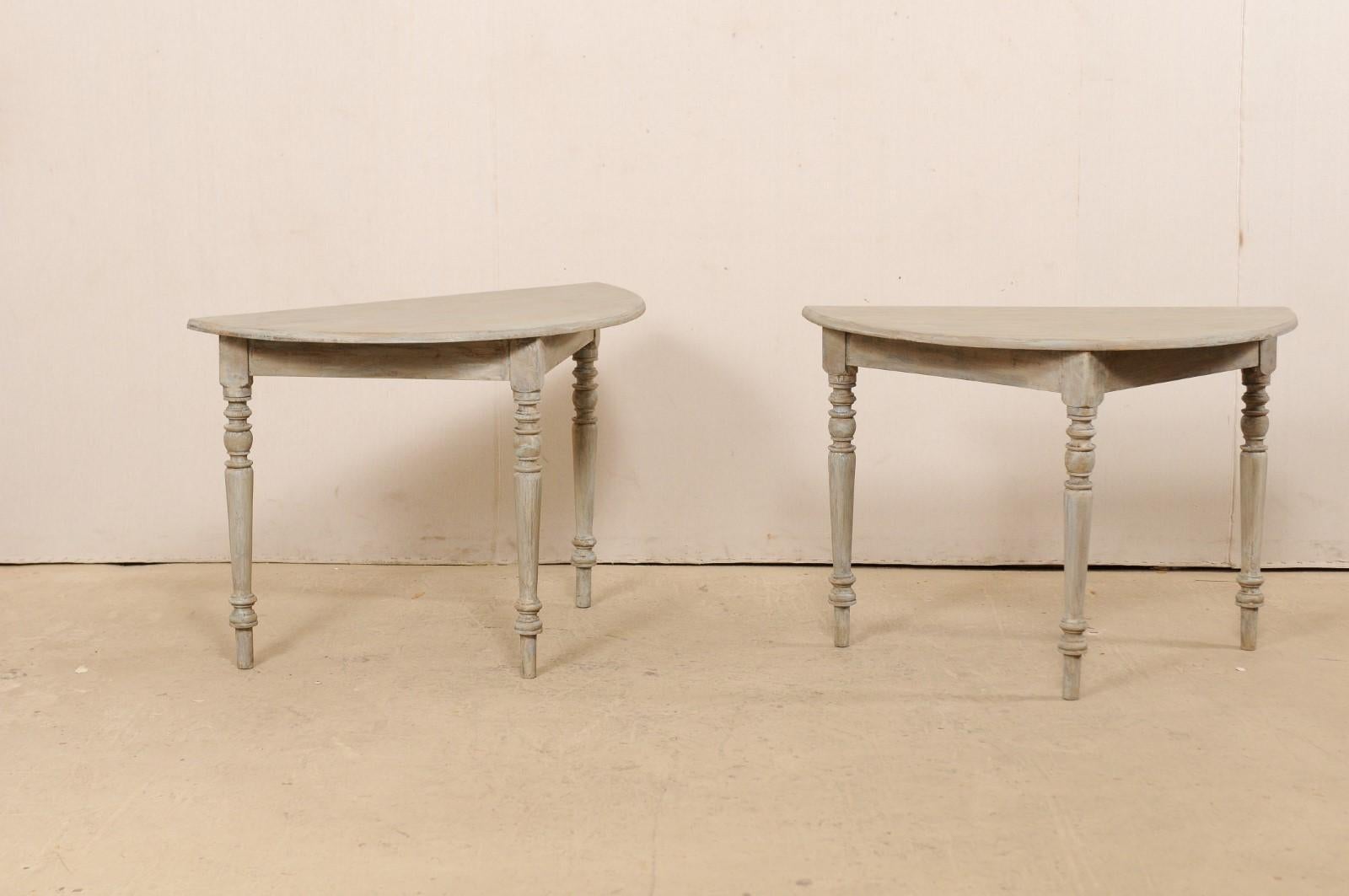 A pair of 19th century Swedish painted wood demilune tables. This pair of antique demilune tables from Sweden each features half moon tops over clean, triangular-shaped aprons, which are raised on three rounded legs with turned carvings accentuating