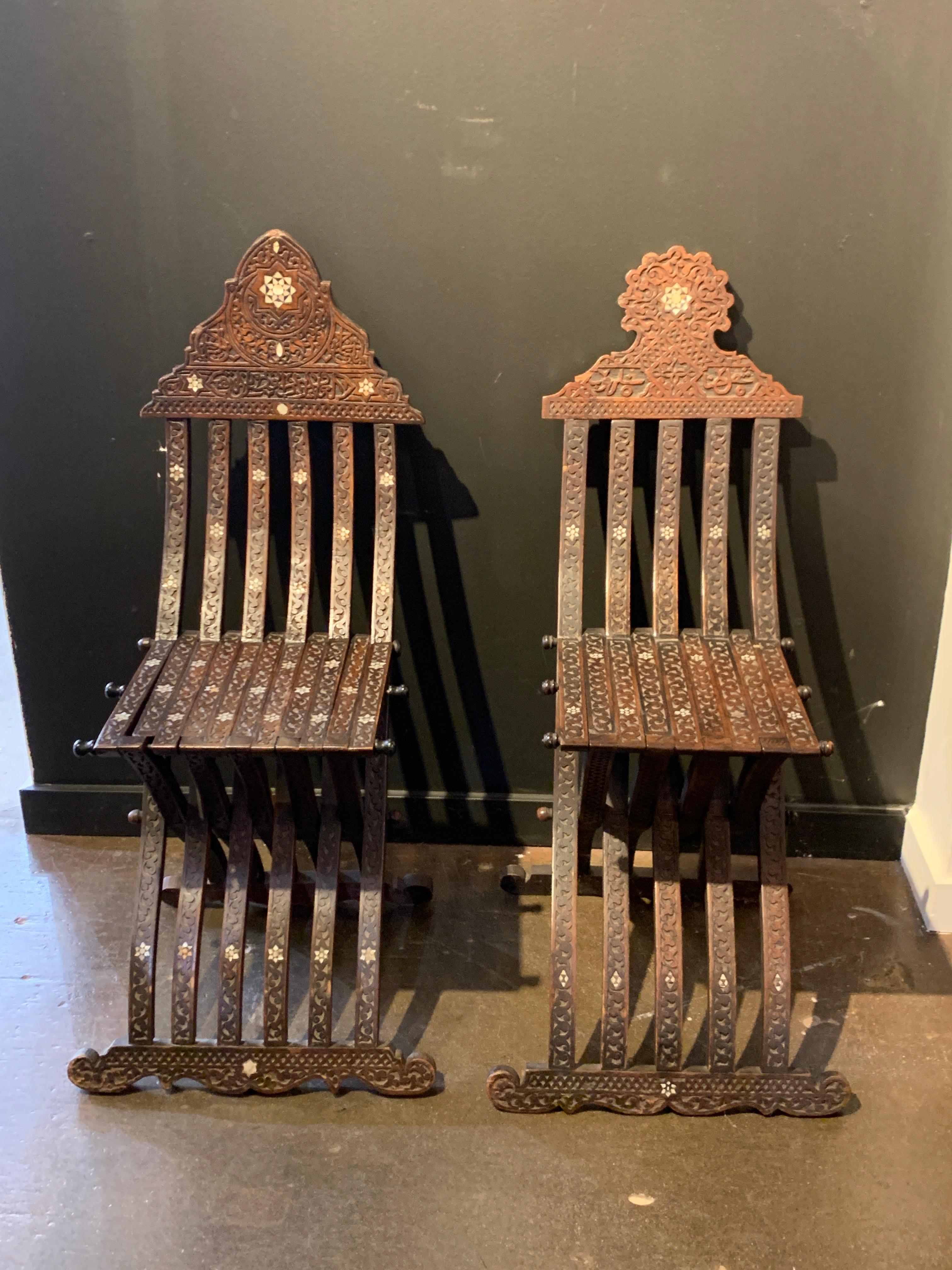 A classic and elegant near pair of antique Syrian carved walnut folding scribes chairs with shell and bone inlay, late 19th century, Syria.

The chairs of hand carved walnut in a folding slat design and set on curule legs. The wood carved with an