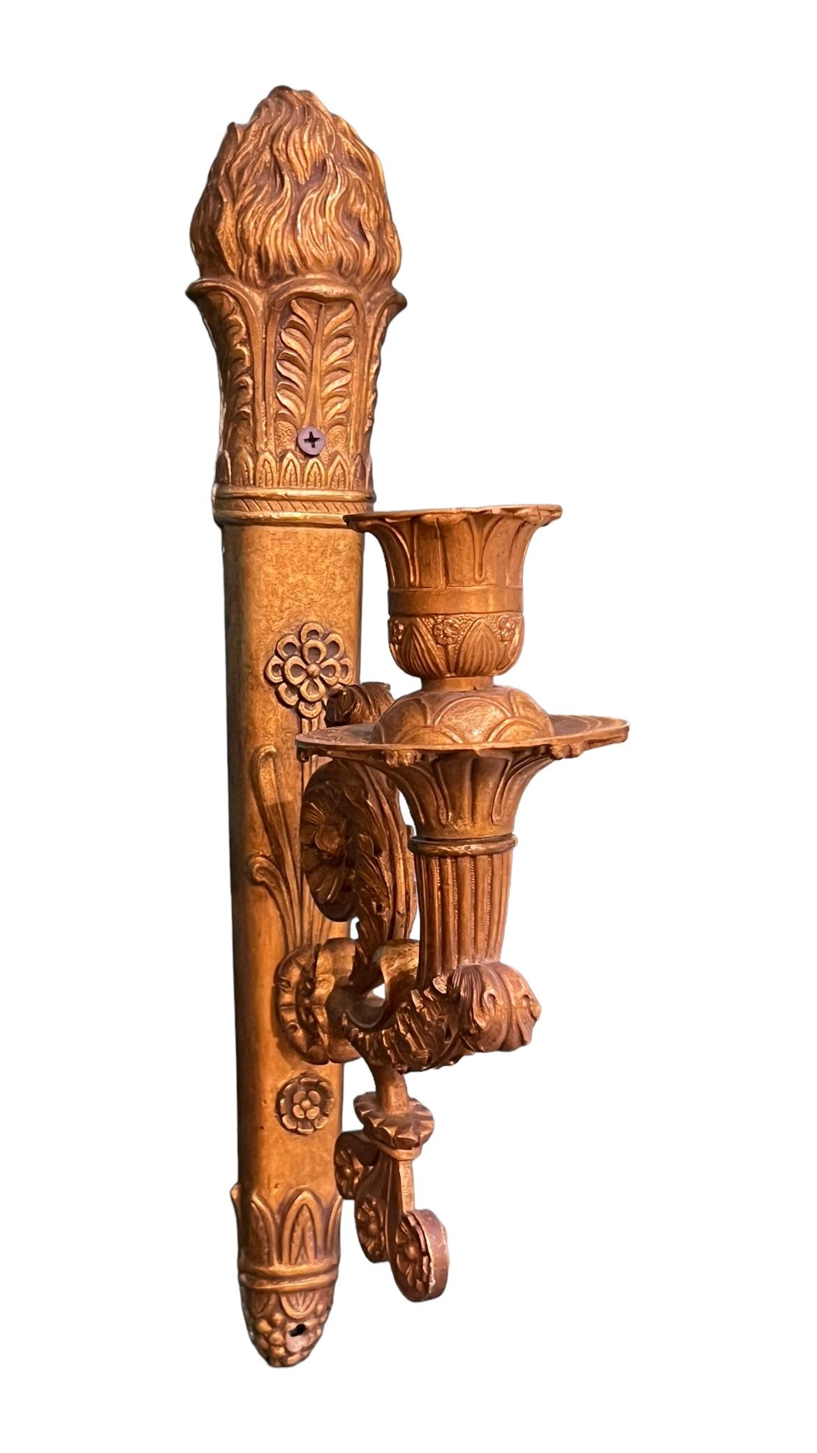 La nostra coppia di appliques antiche (inizio del XX secolo) in metallo in stile neoclassico Antique French Empire ha una piastra posteriore a forma di torcia infuocata e decorata con rosette, anthemions, gadrooning e motivi di scorrimento.  