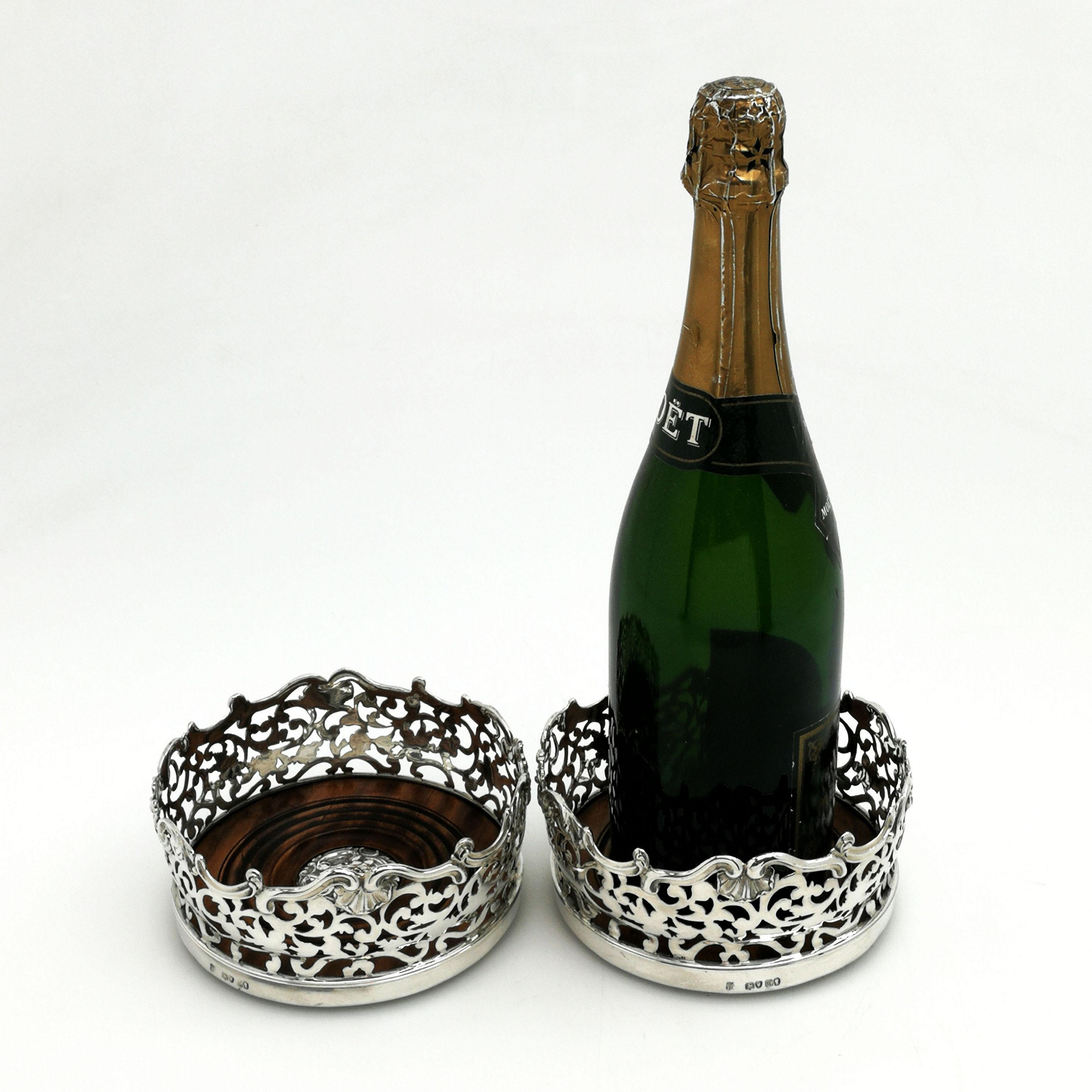 A pair of magnificent Antique solid Silver Wine Bottle Coasters embellished with an ornate pierced pattern around the tall sides of the coaster. The rim of the Coaster has an ornate shell and scroll border and the wooden base of the coaster has an