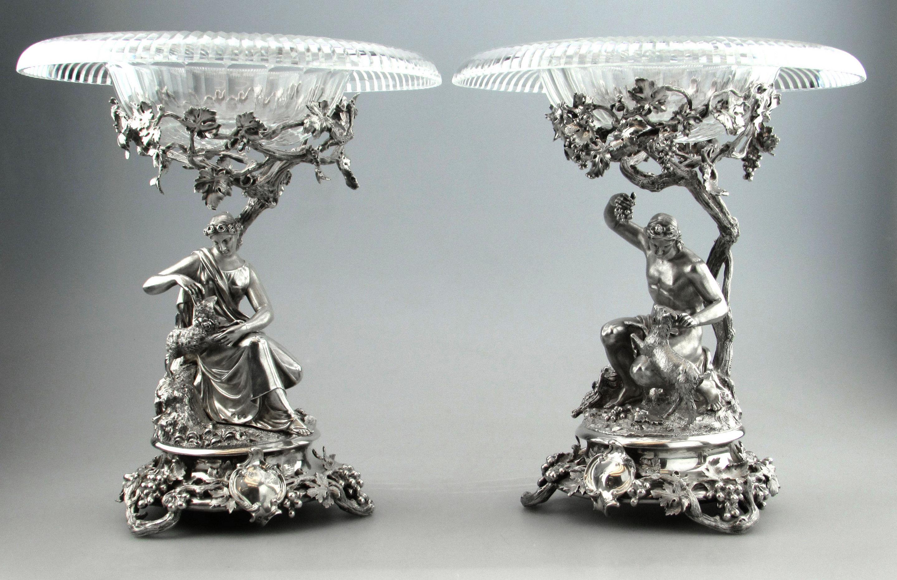 A pair of impressive antique Victorian silver comports with magnificent silver bases supporting elegant cut glass dishes. The silver bases each show a mythological style figure, one of a woman with a lamb beside her and a young man with a goat. The