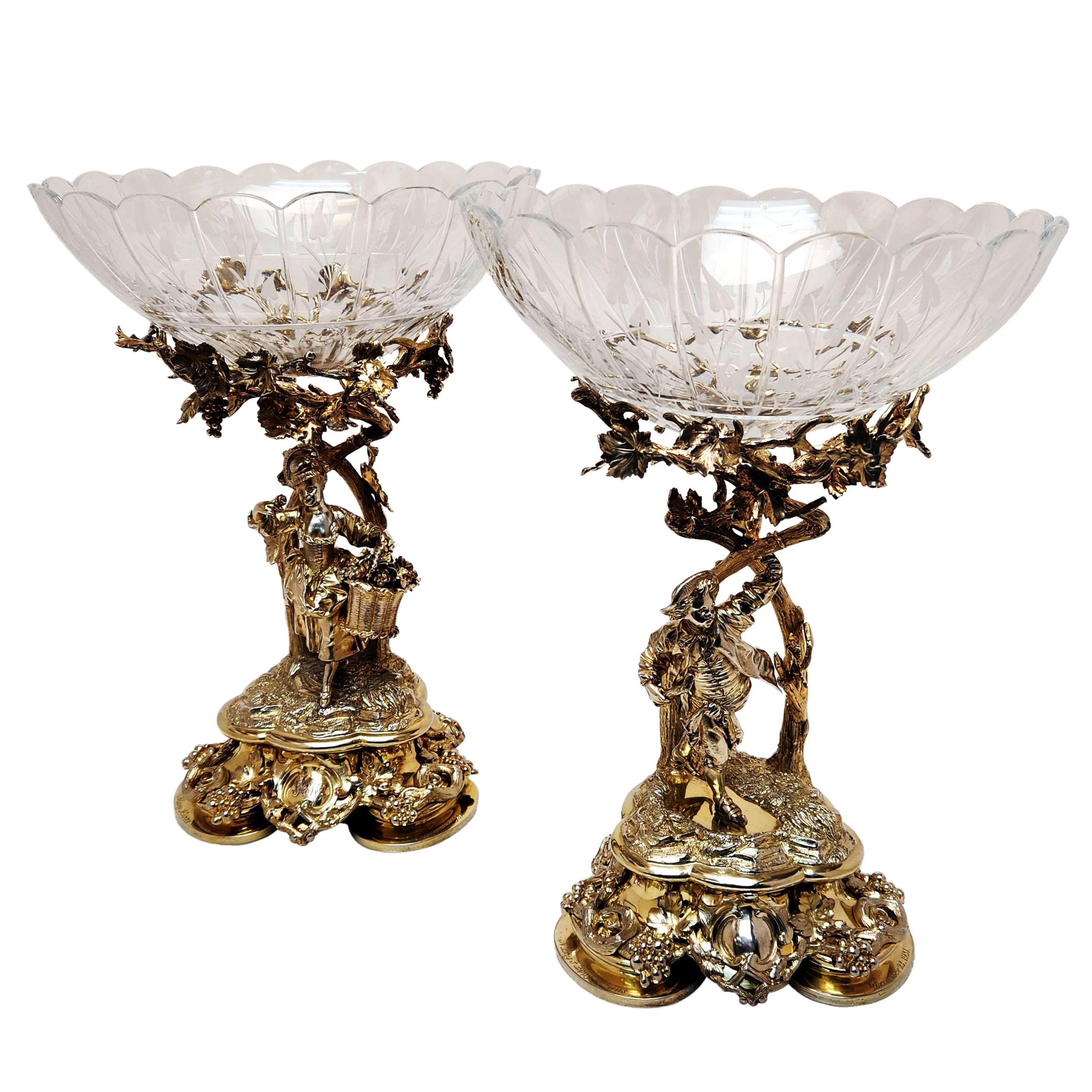 A pair of magnificent Antique Victorian Silver Gilt Comports with cut glass liners. Each Comport has a figure standing below a spread vine bough covered in hanging grapes. One figure is of a lady and one of a man and each figure is wearing period