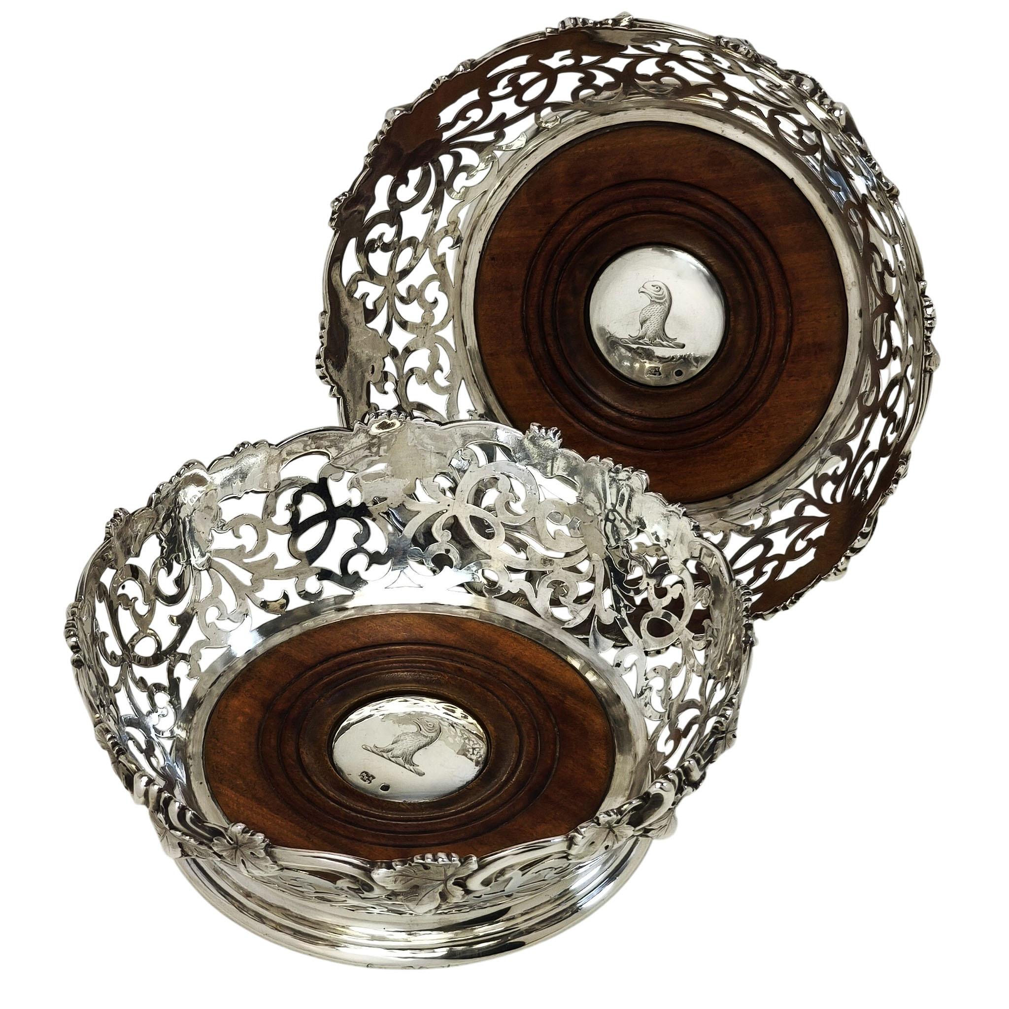 Una splendida coppia di sottobicchieri d'argento vittoriani d'epoca con un bellissimo disegno traforato sui lati e un elegante bordo a forma di uva e vite sul bordo. Le basi sono in legno tornito e ciascuna ha un bottone rotondo al centro con uno